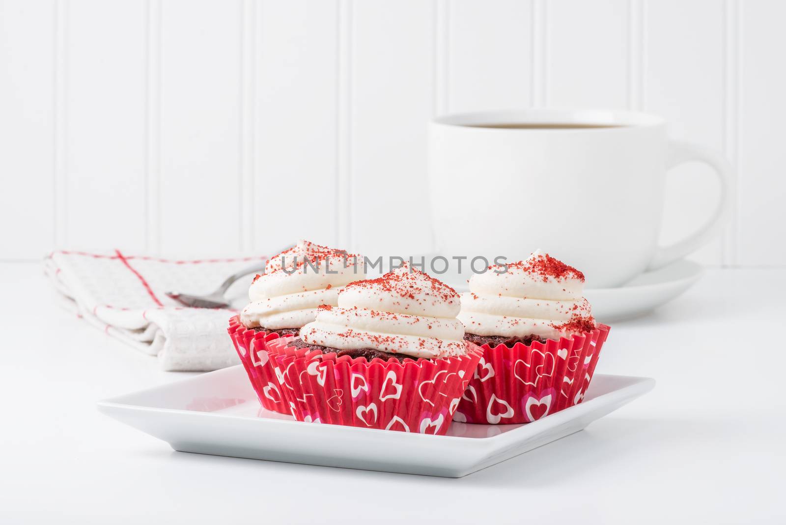 Three red velvet cupcakes served with a cup of coffee.