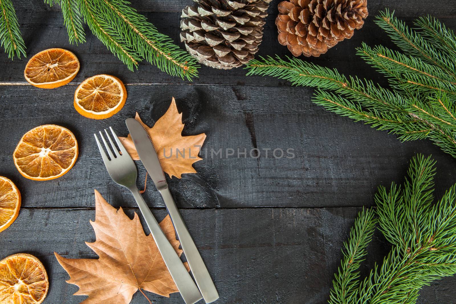 Composition of cutlery on wood background for branches and a decorative dry oranges, pain fruit and leafs for informal dinners or family celebrations in autumn winter season