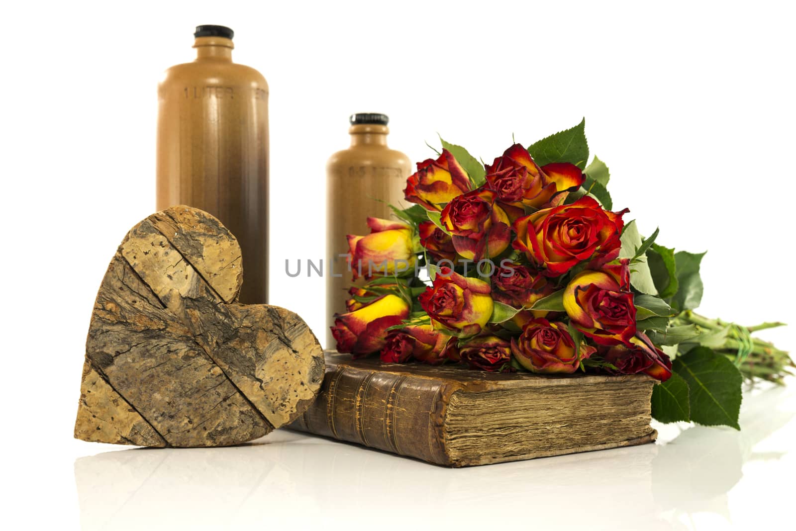 stone bottle with old book and red roses with heart shapes from wood