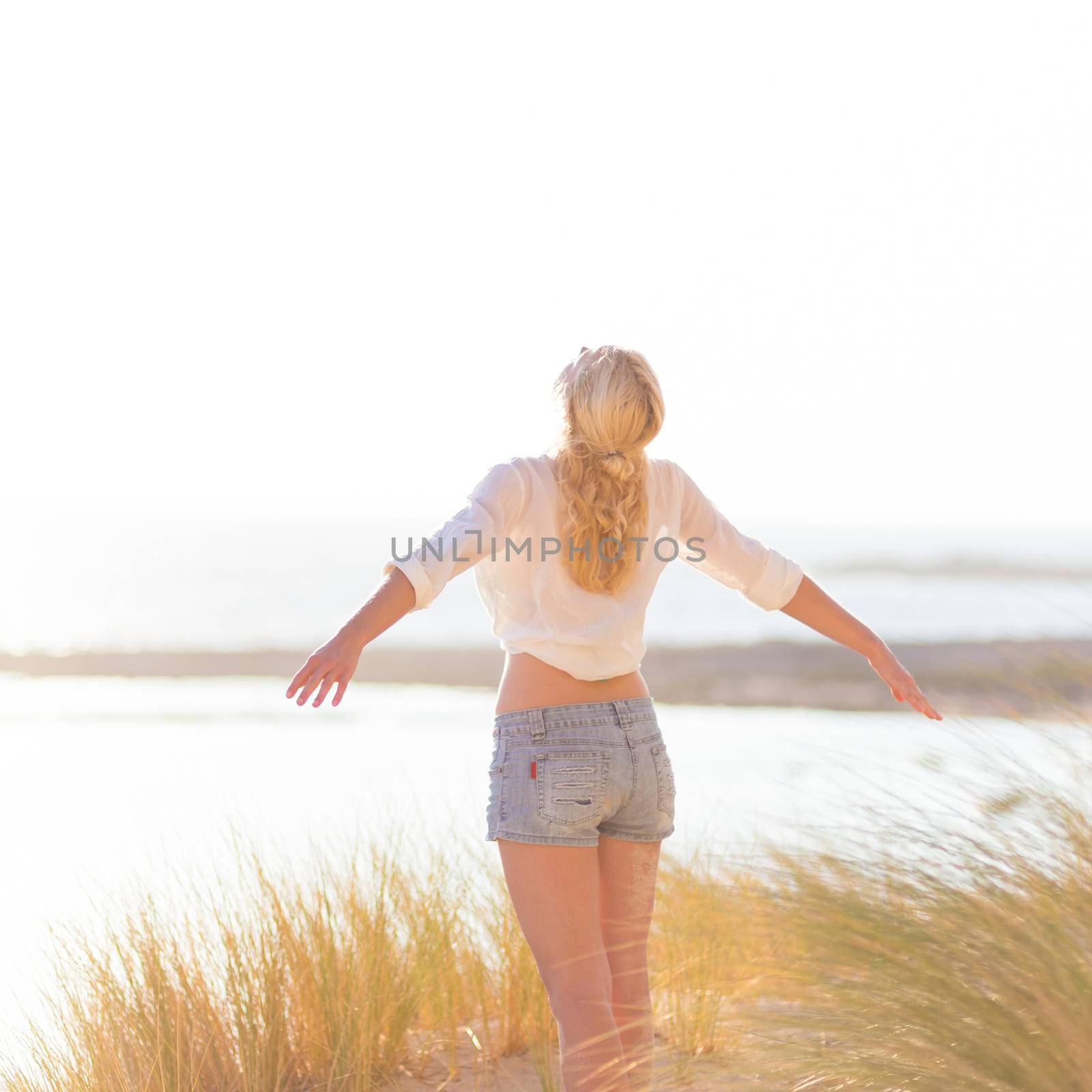 Relaxed woman enjoying freedom and life an a beautiful sandy beach.  Young lady feeling free, relaxed and happy. Concept of happiness, enjoyment and well being.  Enjoying Sun on Vacations. Copyspace.