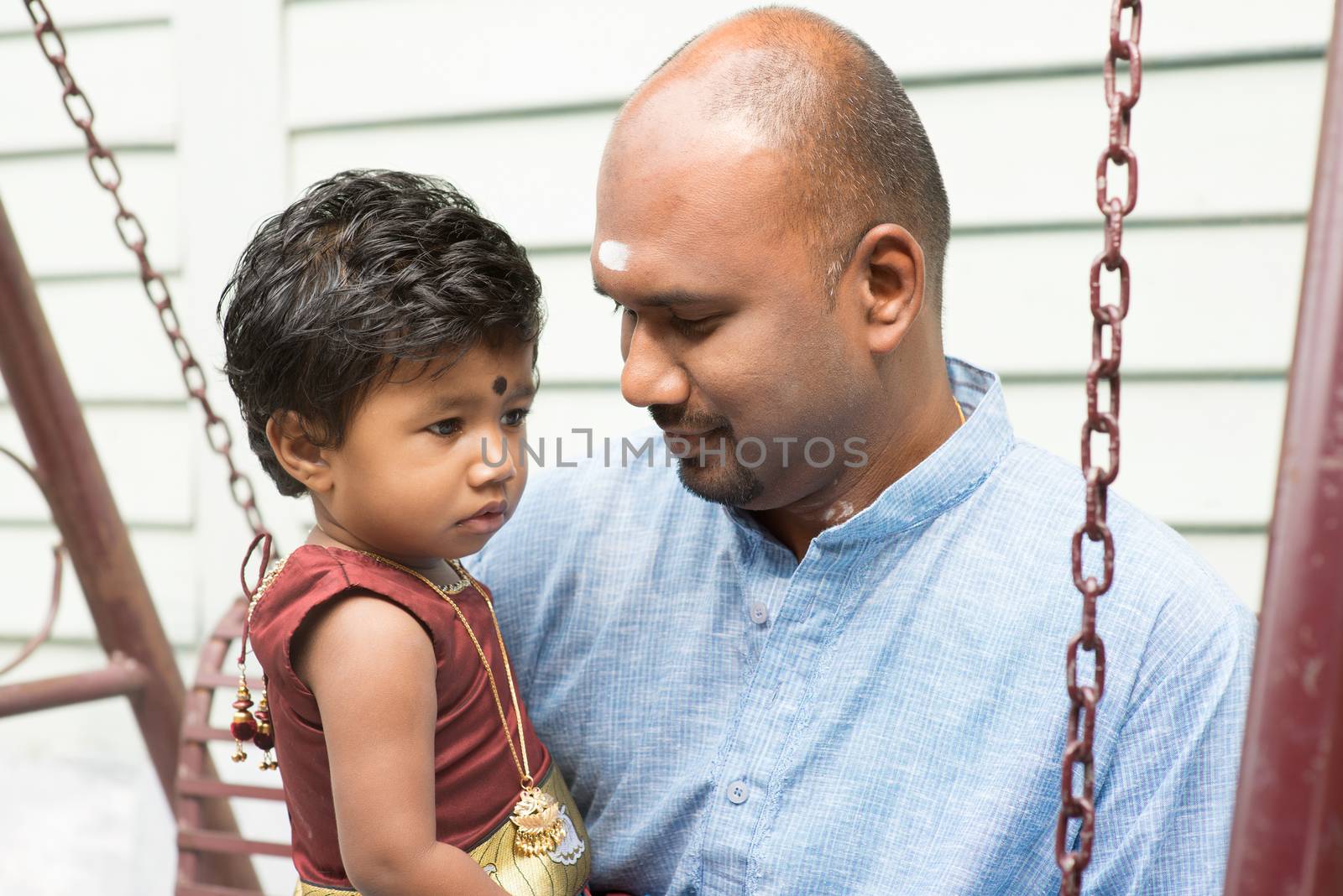 Traditional India family outdoor portrait. Indian father and daughter sitting on a swing. 