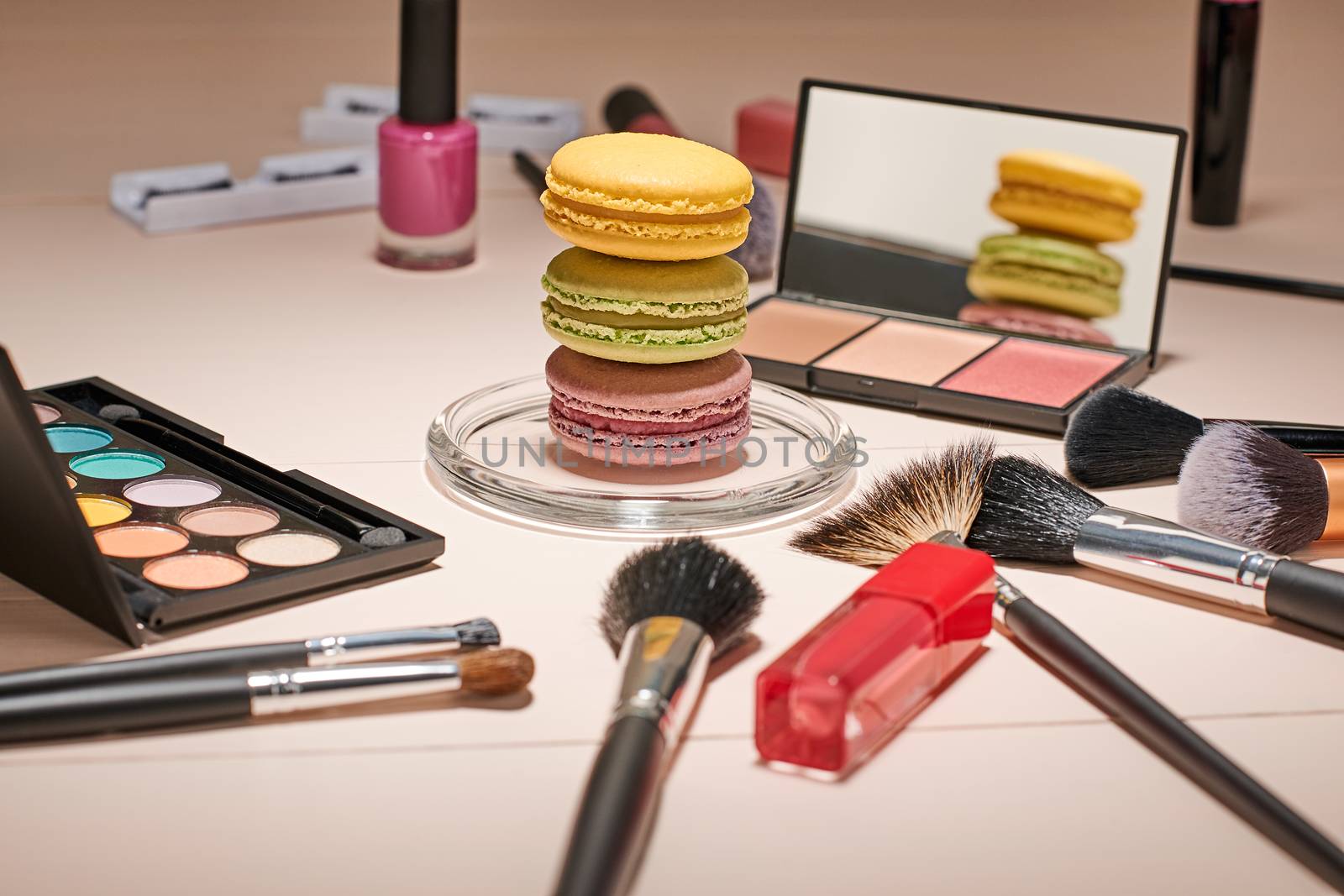 Still life, fashion woman essentials cosmetics. Beauty makeup accessories. Macarons french dessert. Lipstick, brushes, eyeshadow, false eyelashes, mascara.Unusual creative set. Vanilla wood background