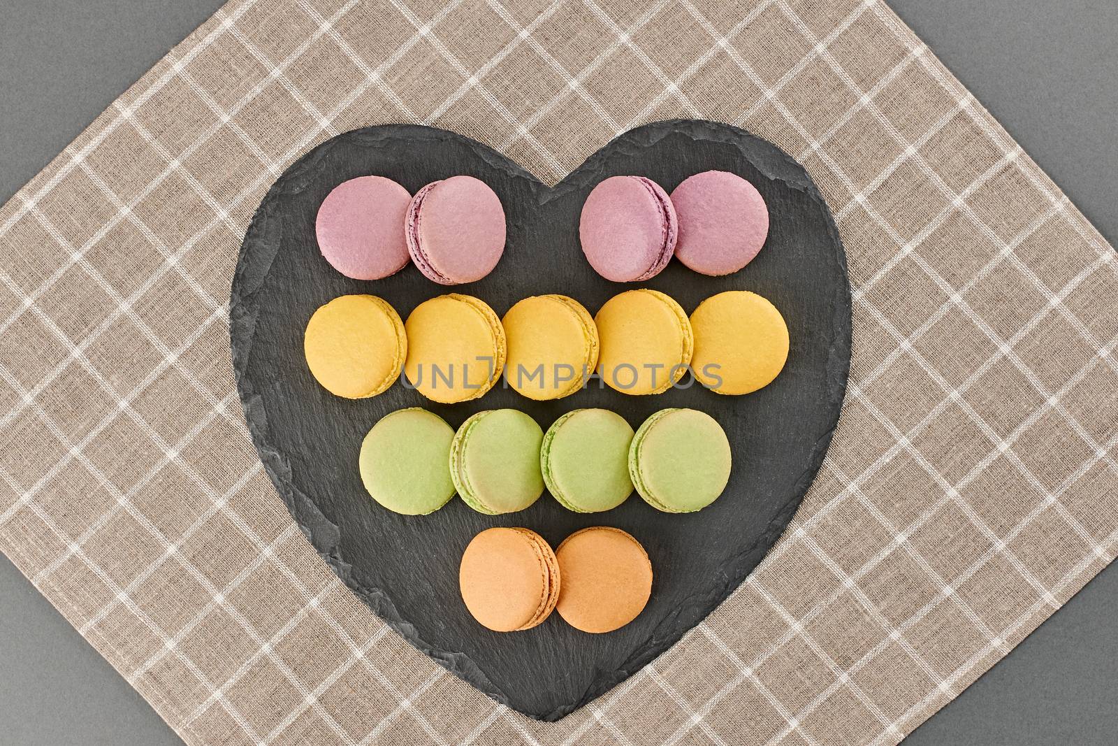 Still life, macarons sweet colorful, heart shape, black placemat. French traditional delicious dessert. Unusual creative romantic, gray background. Concept for love story.Valentines Day