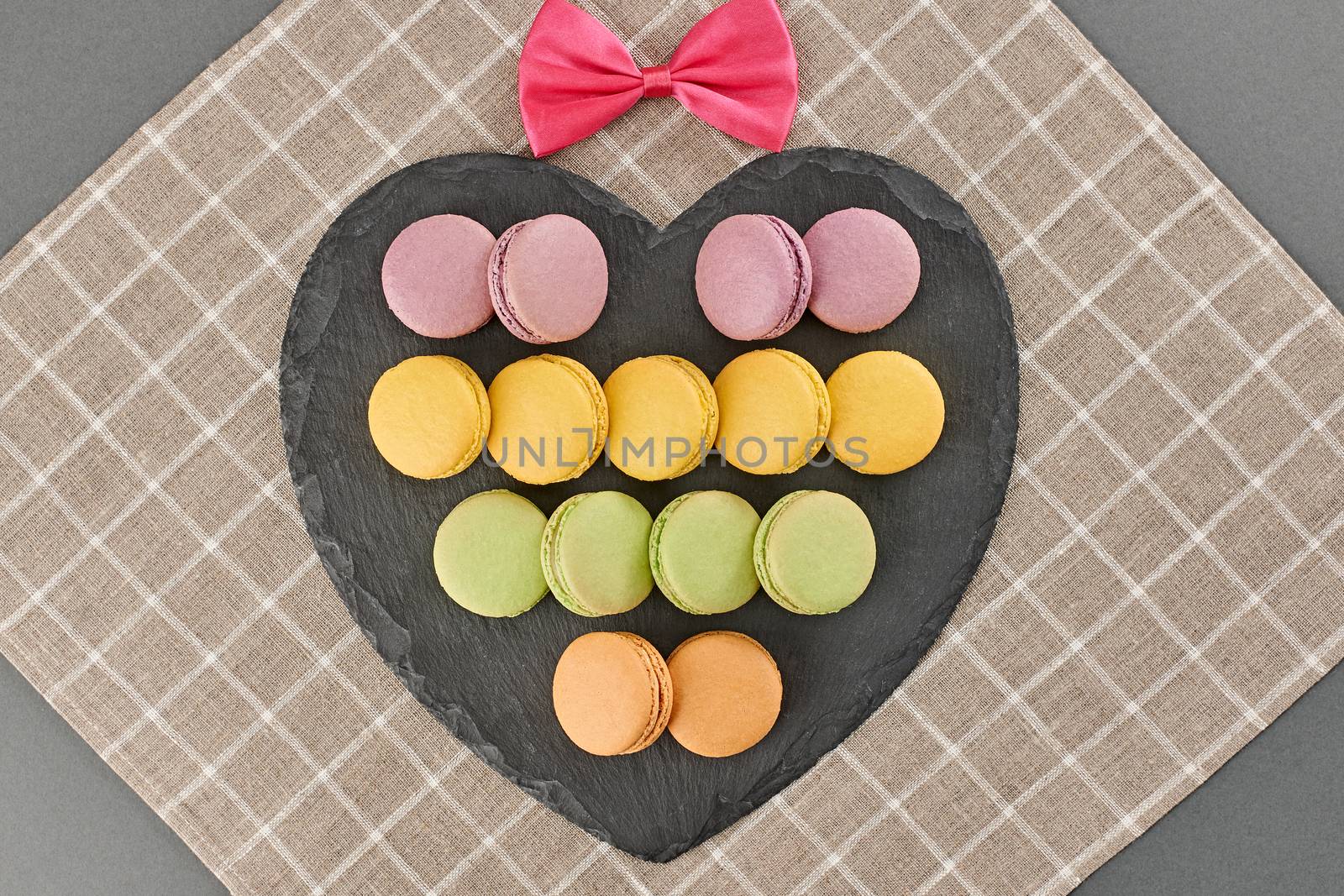 Still life, macarons sweet colorful, black placemat, pink bow. Fresh pastel french traditional dessert. Unusual creative romantic, background. Concept love story. Valentines Day.