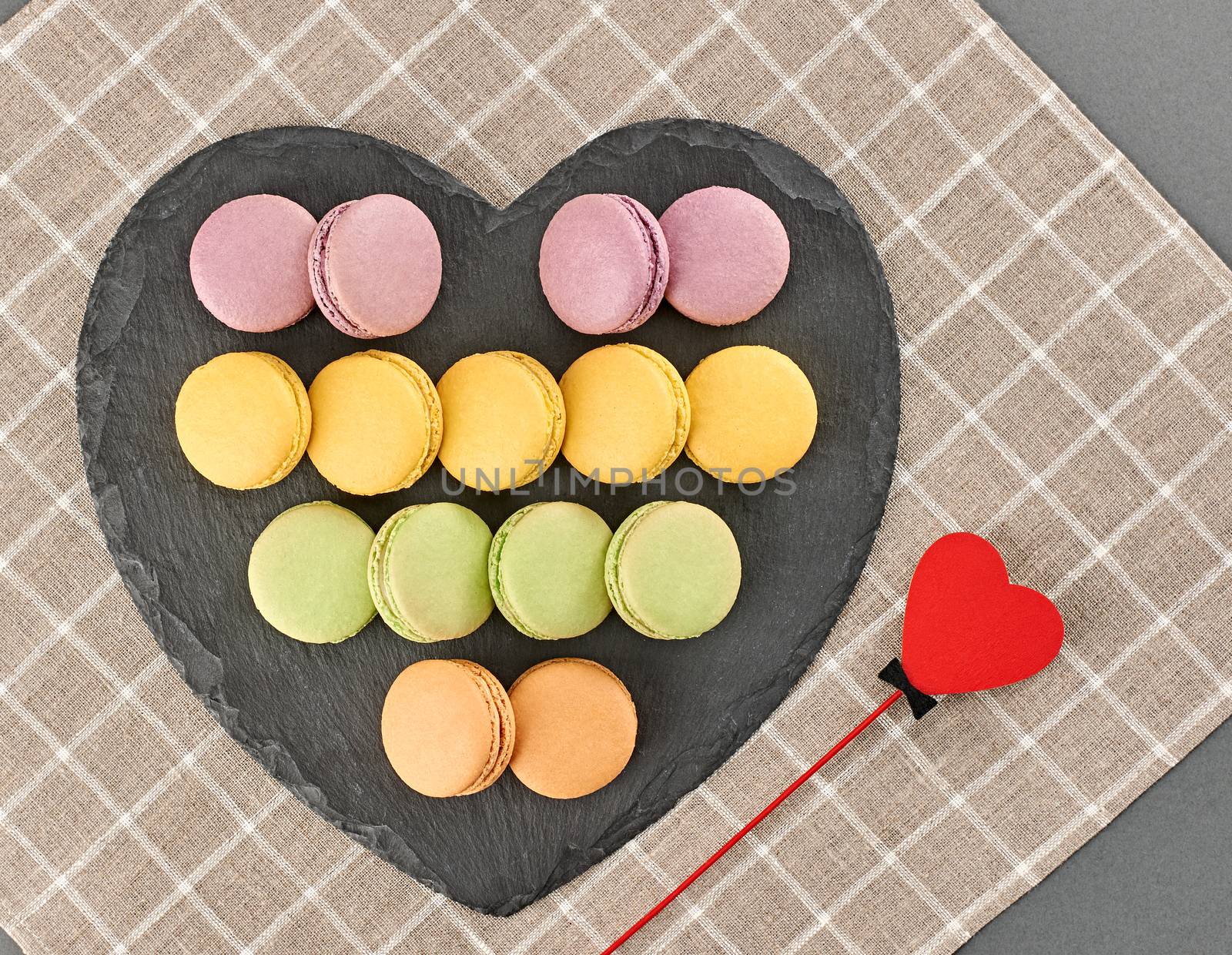 Still life, macarons sweet colorful, black placemat. Heart made of red wood. Fresh pastel french traditional dessert. Unusual creative romantic, background. Concept love story. Valentines Day.
