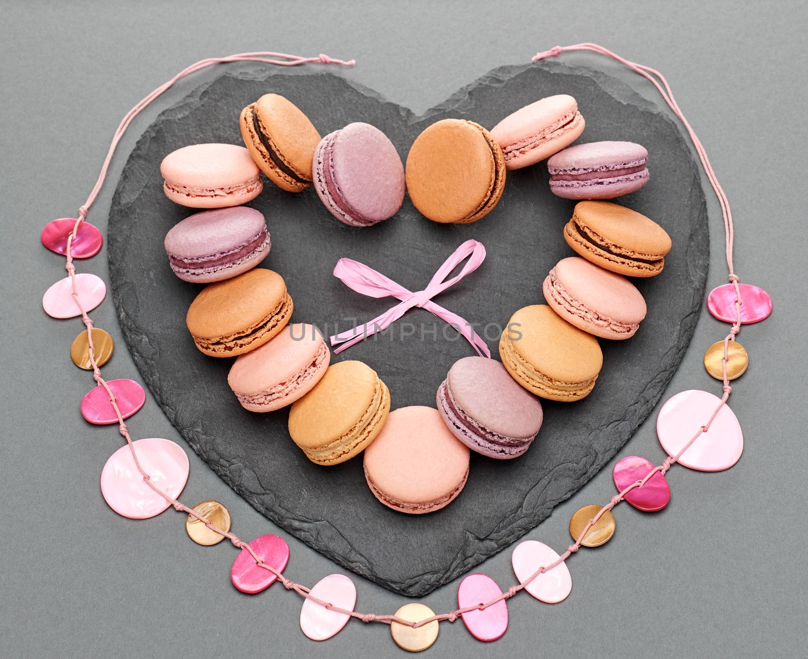 Still life, macarons sweet colorful, heart shape, black placemat. French traditional delicious dessert, necklace, bow. Unusual creative romantic, gray background. Concept for love story.Valentines Day