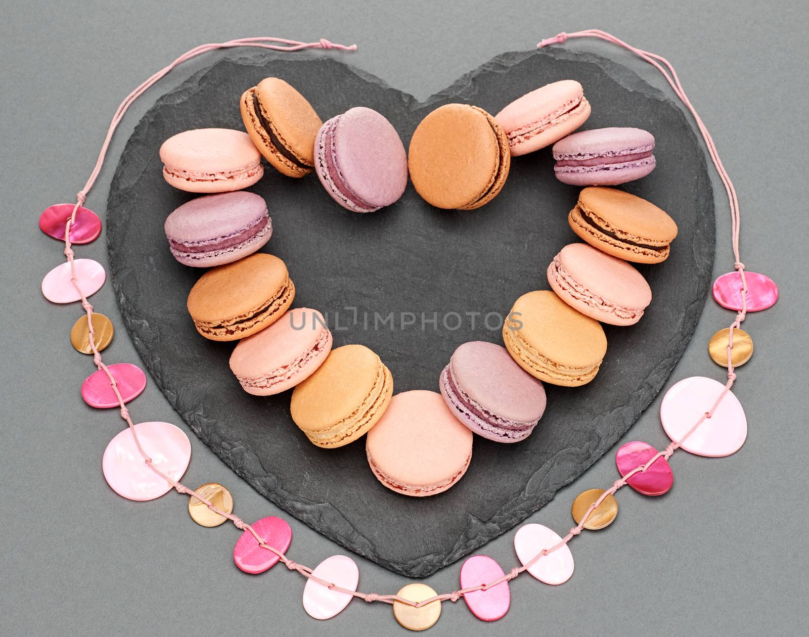 Still life, macarons sweet colorful, heart shape, black placemat. French traditional delicious dessert with necklace. Unusual creative romantic, gray background. Concept for love story.Valentines Day