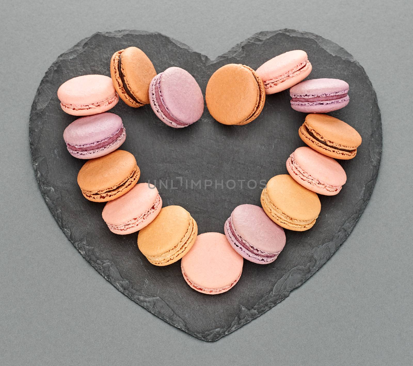 Still life, macarons sweet colorful, heart shape, black placemat. French traditional delicious dessert. Unusual creative romantic, gray background. Concept for love story.Valentines Day