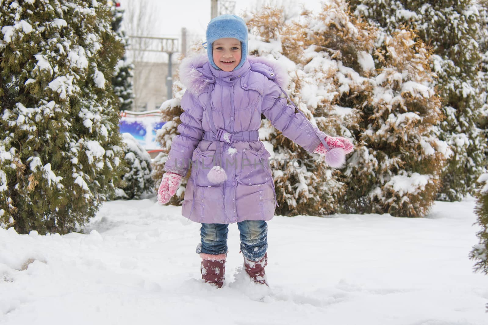 Five-year girl costs on a snowdrift snow against a snowy background Trees