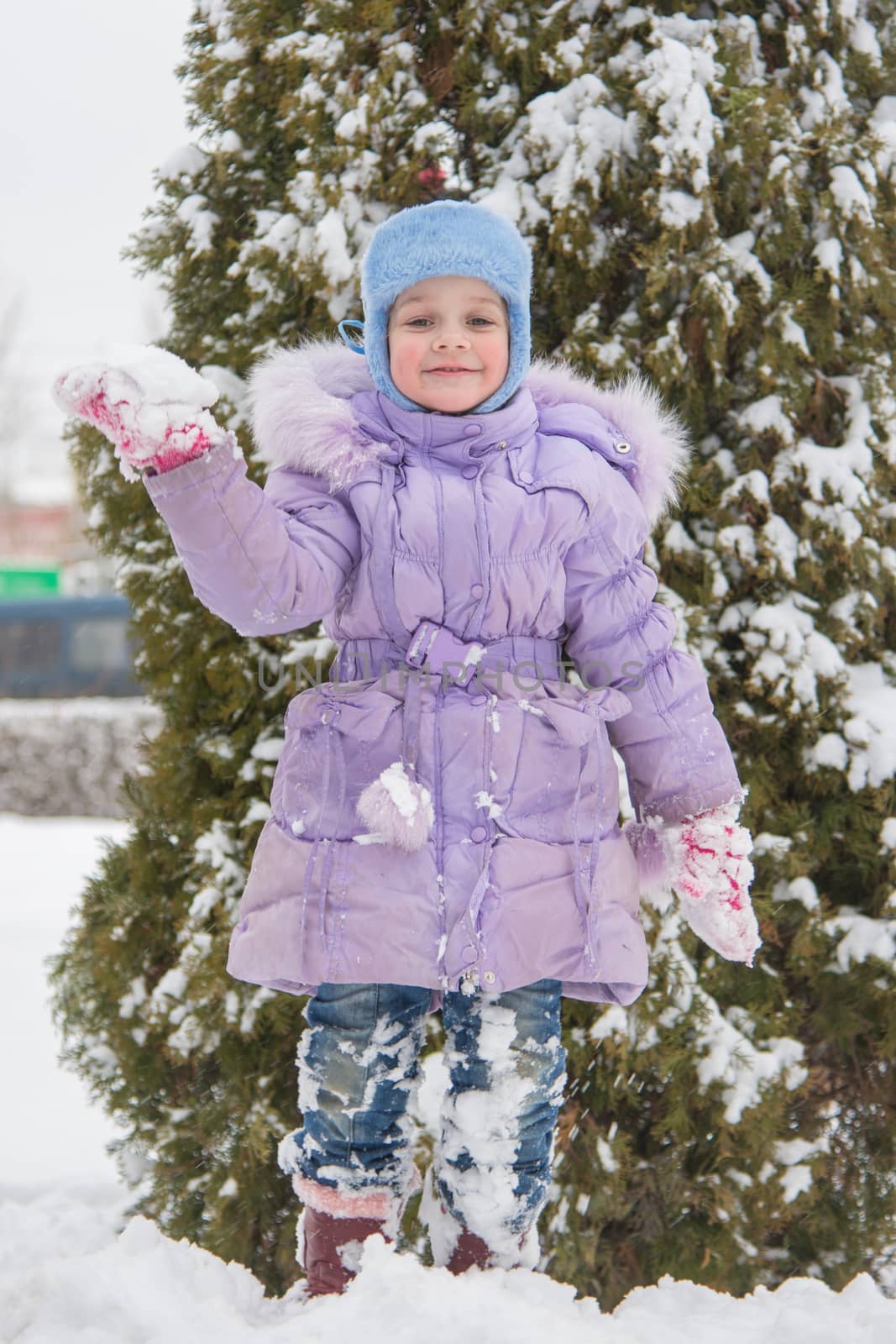 Five-year girl costs on a snowdrift snow against a snowy background Trees