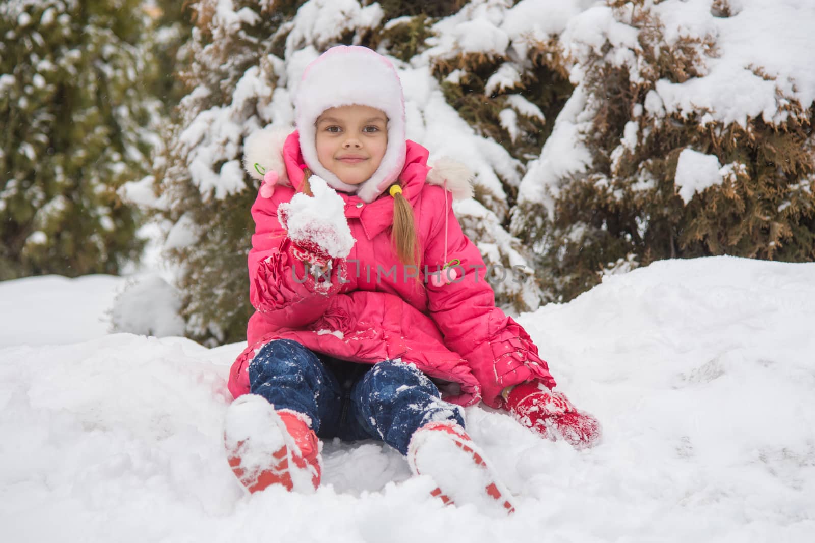 Seven-year girl sitting in a snowdrift snow against a snowy background Trees