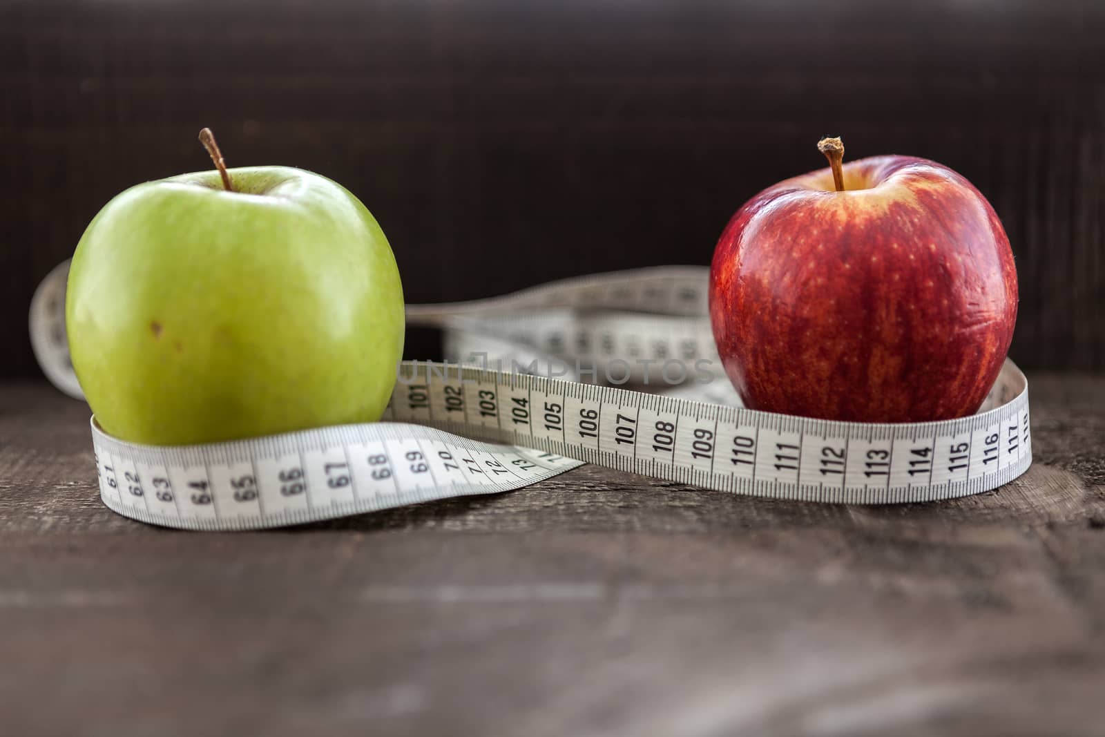 The image shows apple surrounded by a measuring tape referring to diet and health concept on wooden background