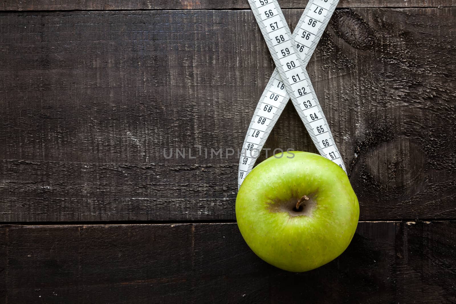 The image shows apple surrounded by a measuring tape referring to diet and health concept on wooden background