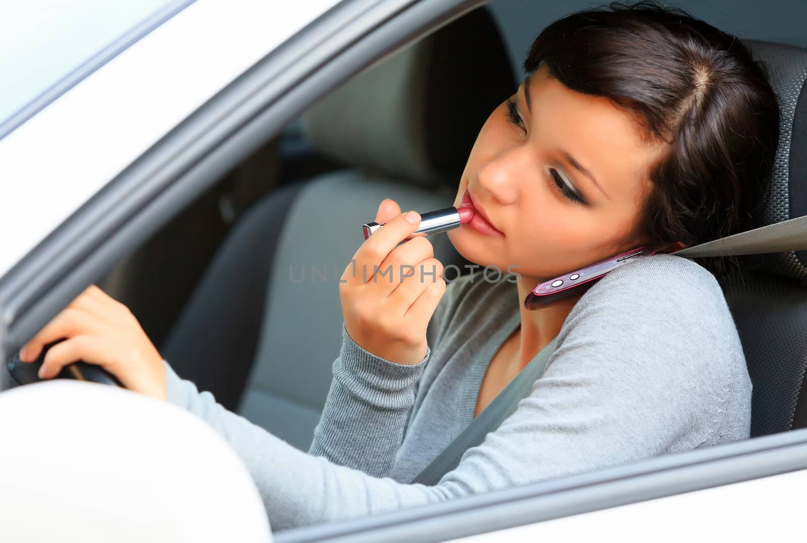 Female driver talking by mobile telephone and doing make-up. by Nobilior