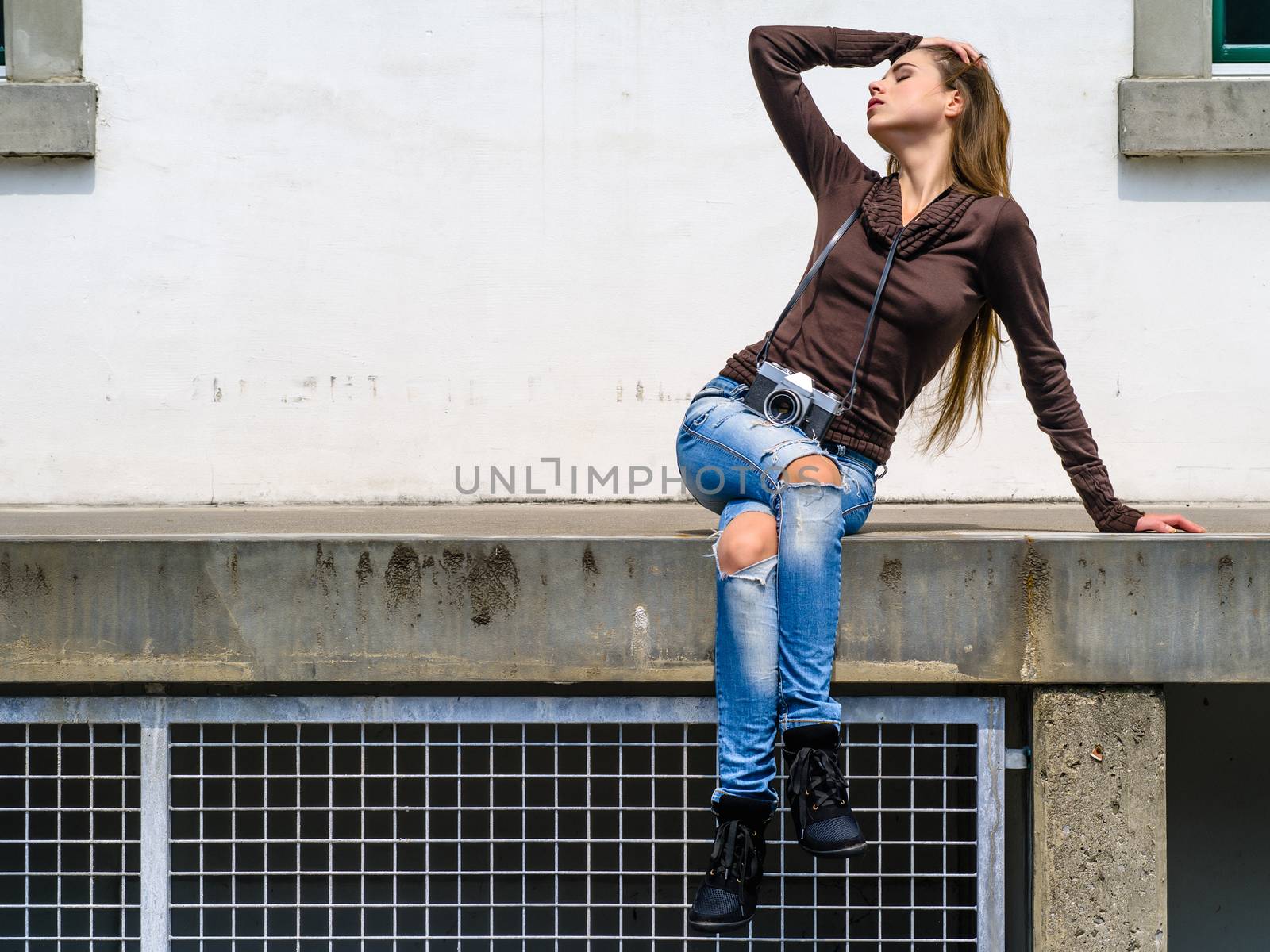 Photo of a sexy young woman in the city with her eyes closed enjoying the sunlight and holding a vintage camera.