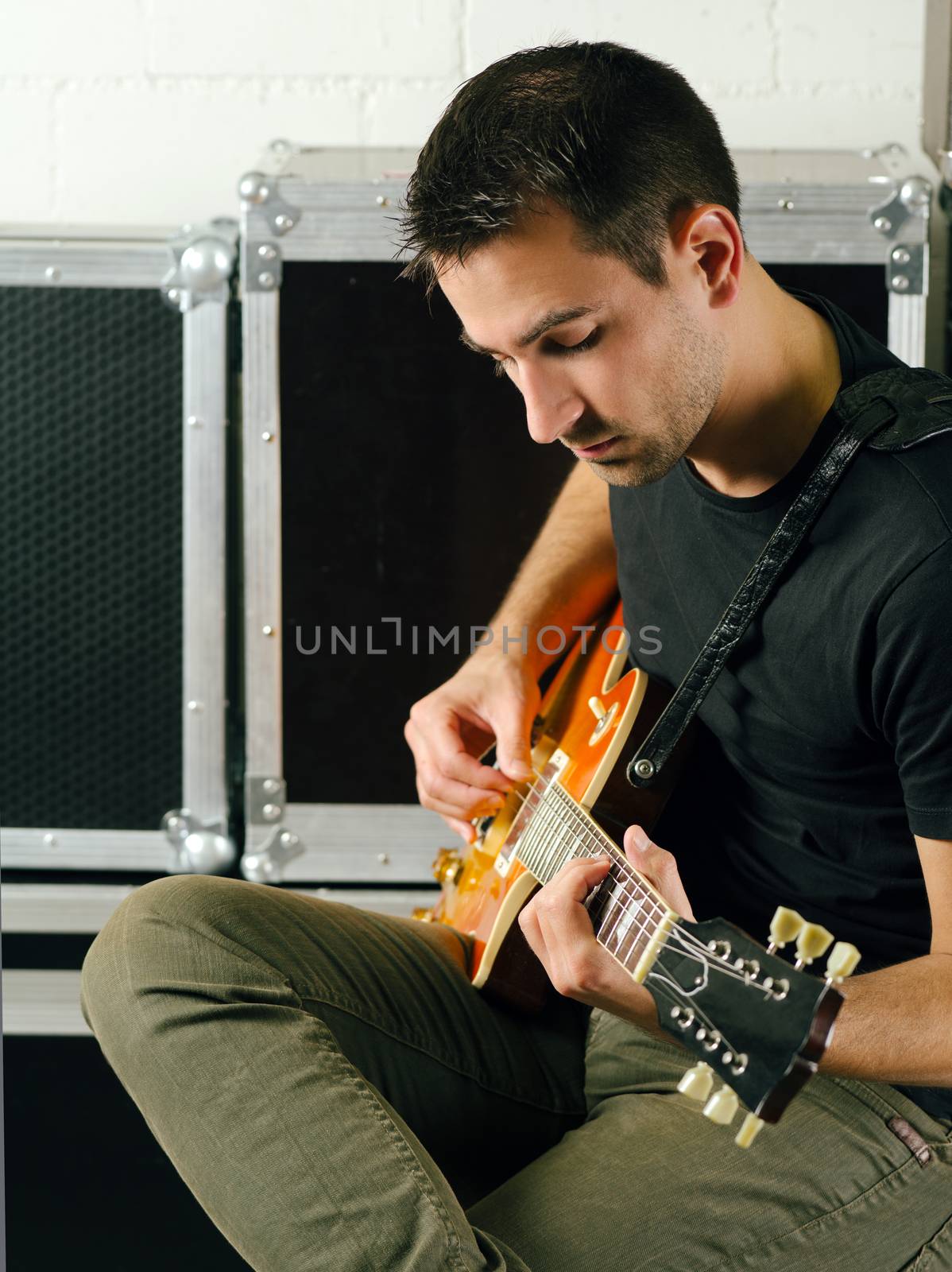 Photo of a man sitting backstage practicing his guitar.