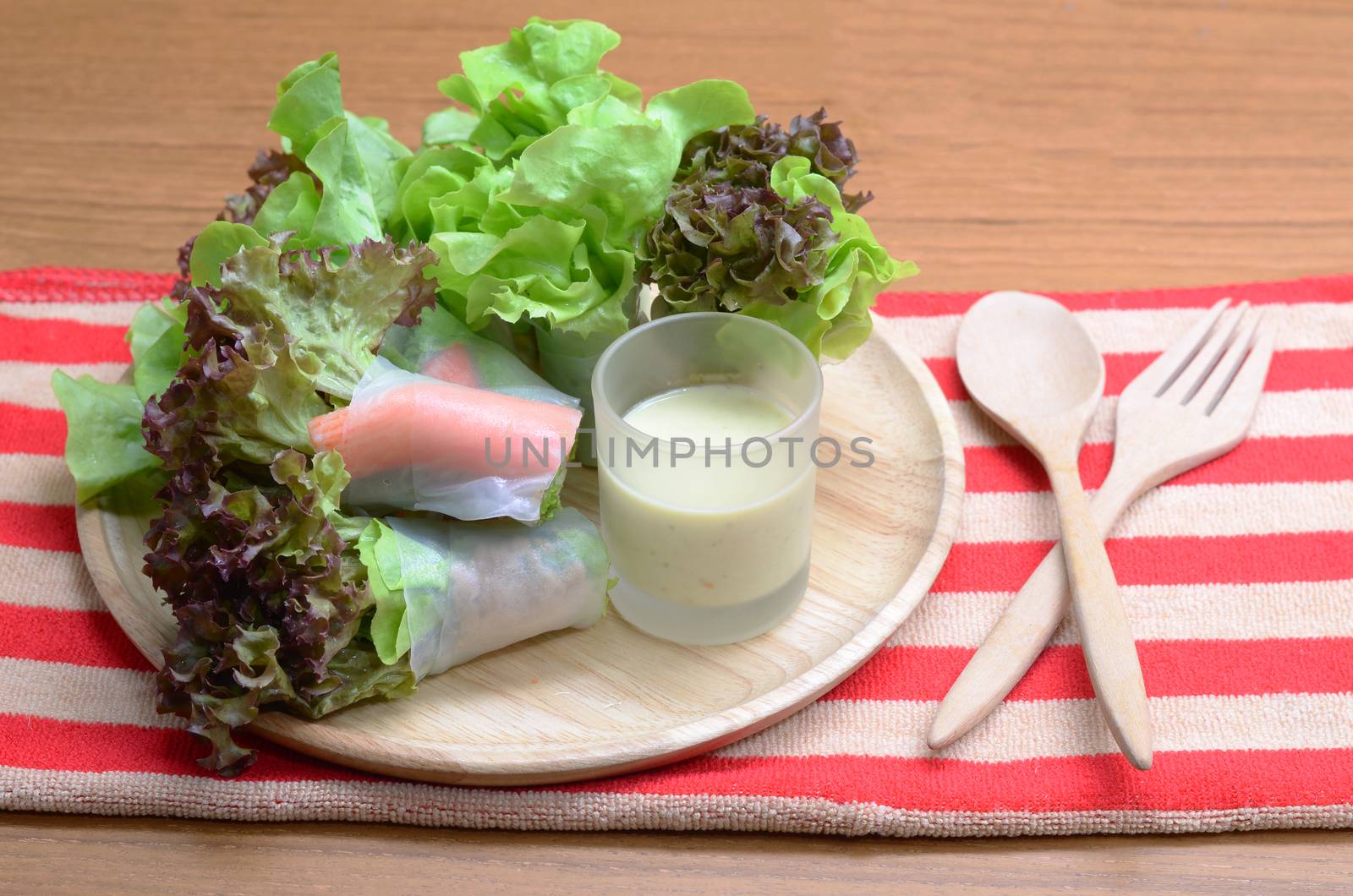 Salad roll vegetables and crab stick with salad dressing in wooden plate, folk and spoon.