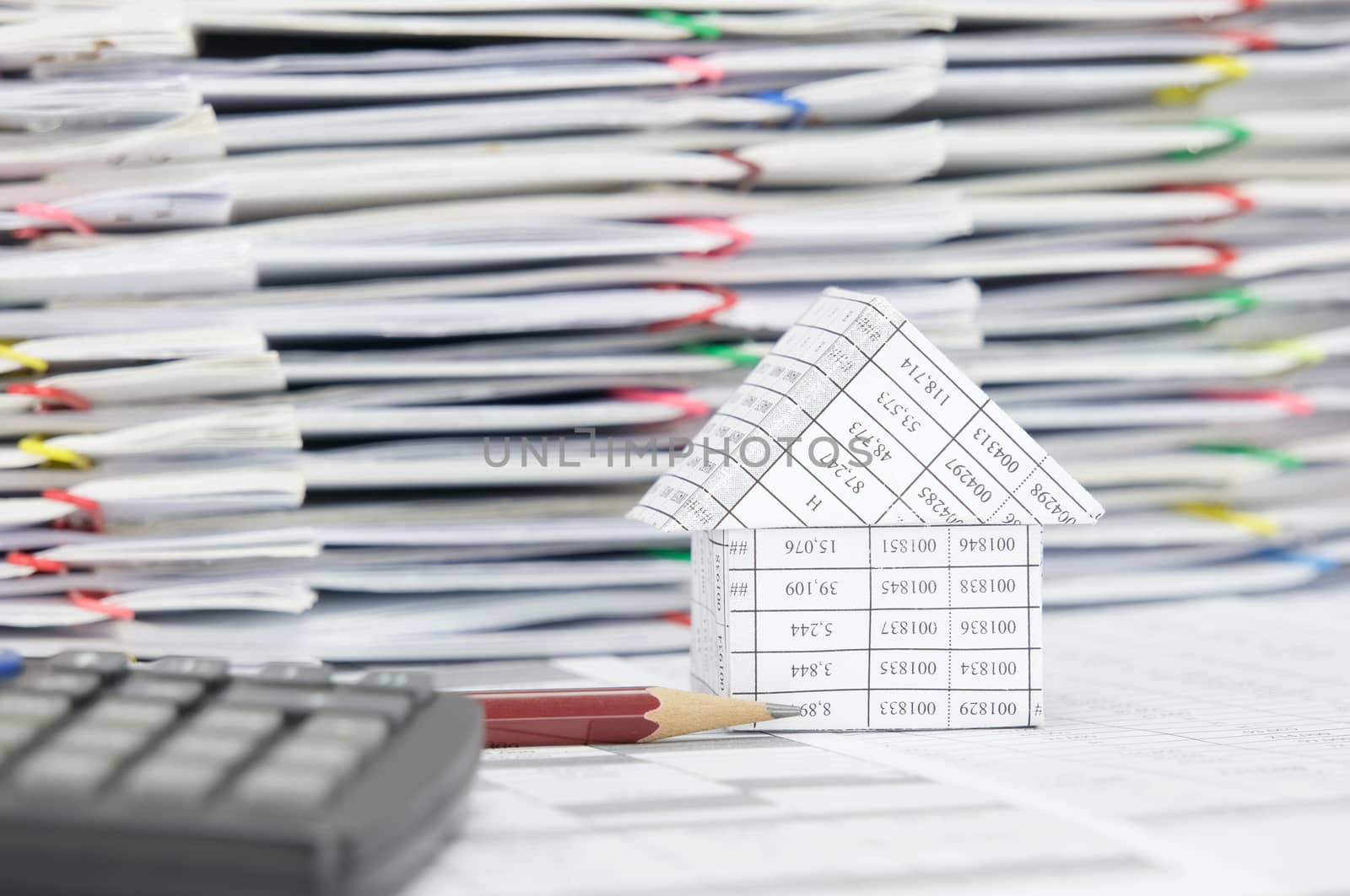 Close up brown pencil and house on finance account have blur calculator and pile of document with colorful paperclip as foreground and background.