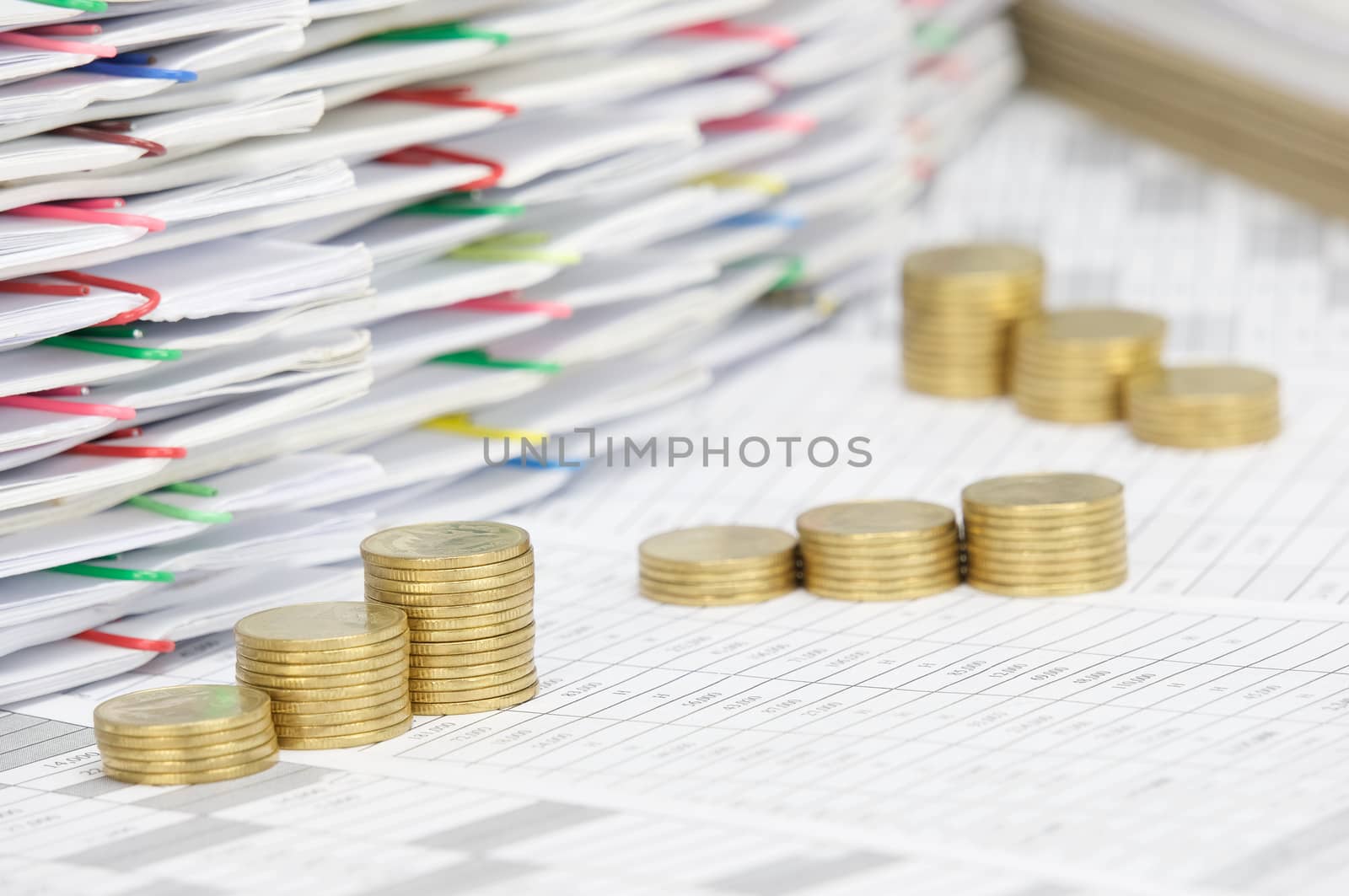 Step pile of gold coins on finance account have pile of document with colorful paperclip and brown envelope as background.