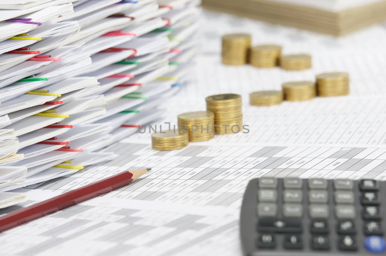 Brown pencil on finance account have blur calculator and step pile of gold coins and pile of document with colorful paperclip and brown envelope as foreground and background.