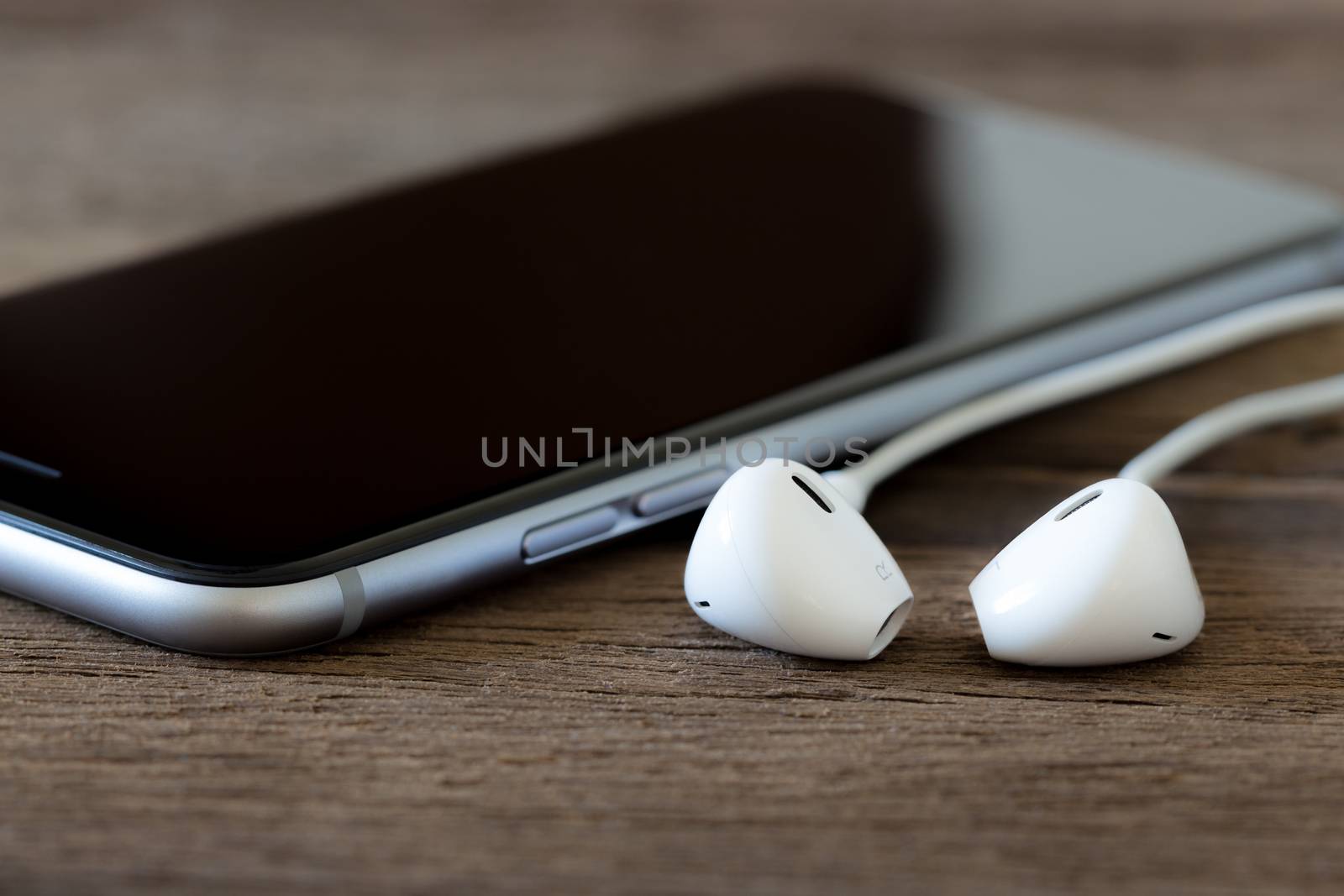 closeup phone and earbud on wood desk by blackzheep