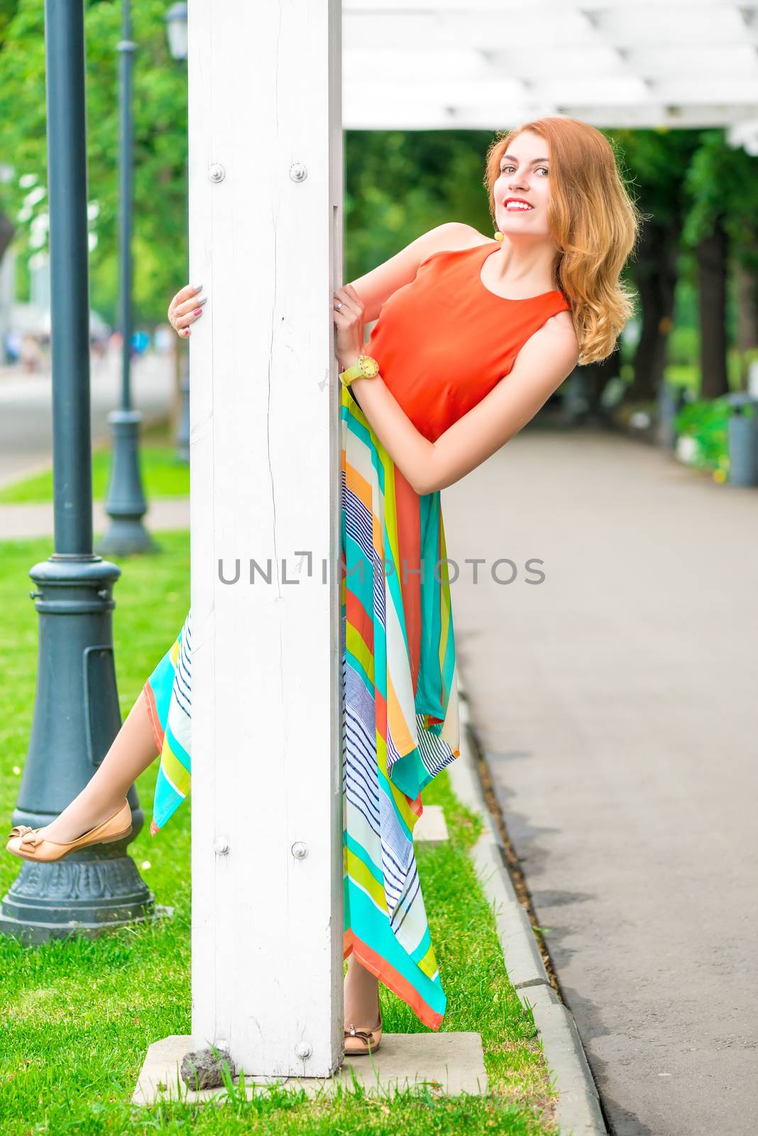 cheerful girl looks out from behind pillar gazebo in the park