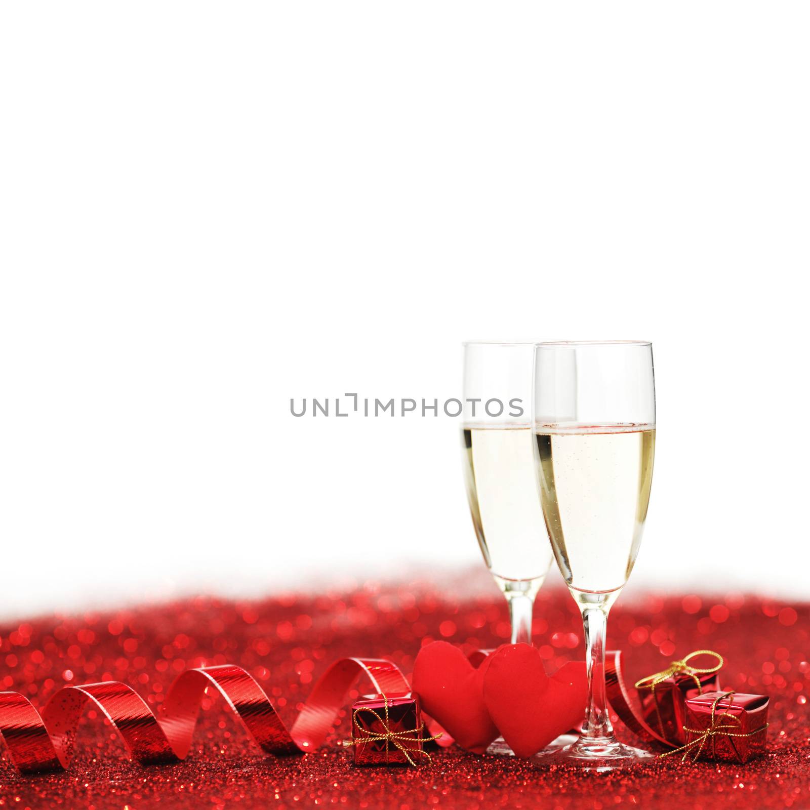 Glasses with Champagne and handmade hearts on red glitters isolated on white background