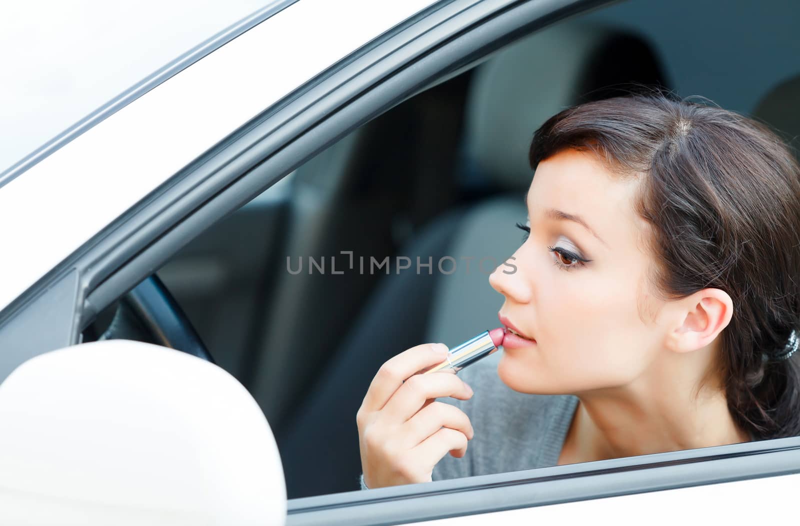 Young brunette woman applying makeup while in the car by Nobilior