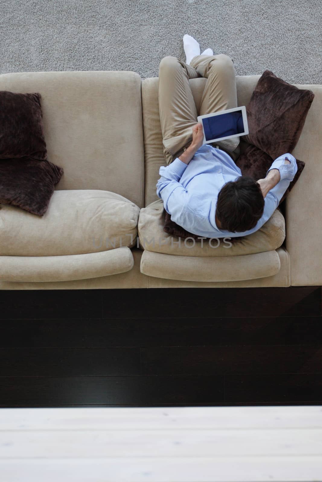 Man surfing on tablet on a couch at home, top view