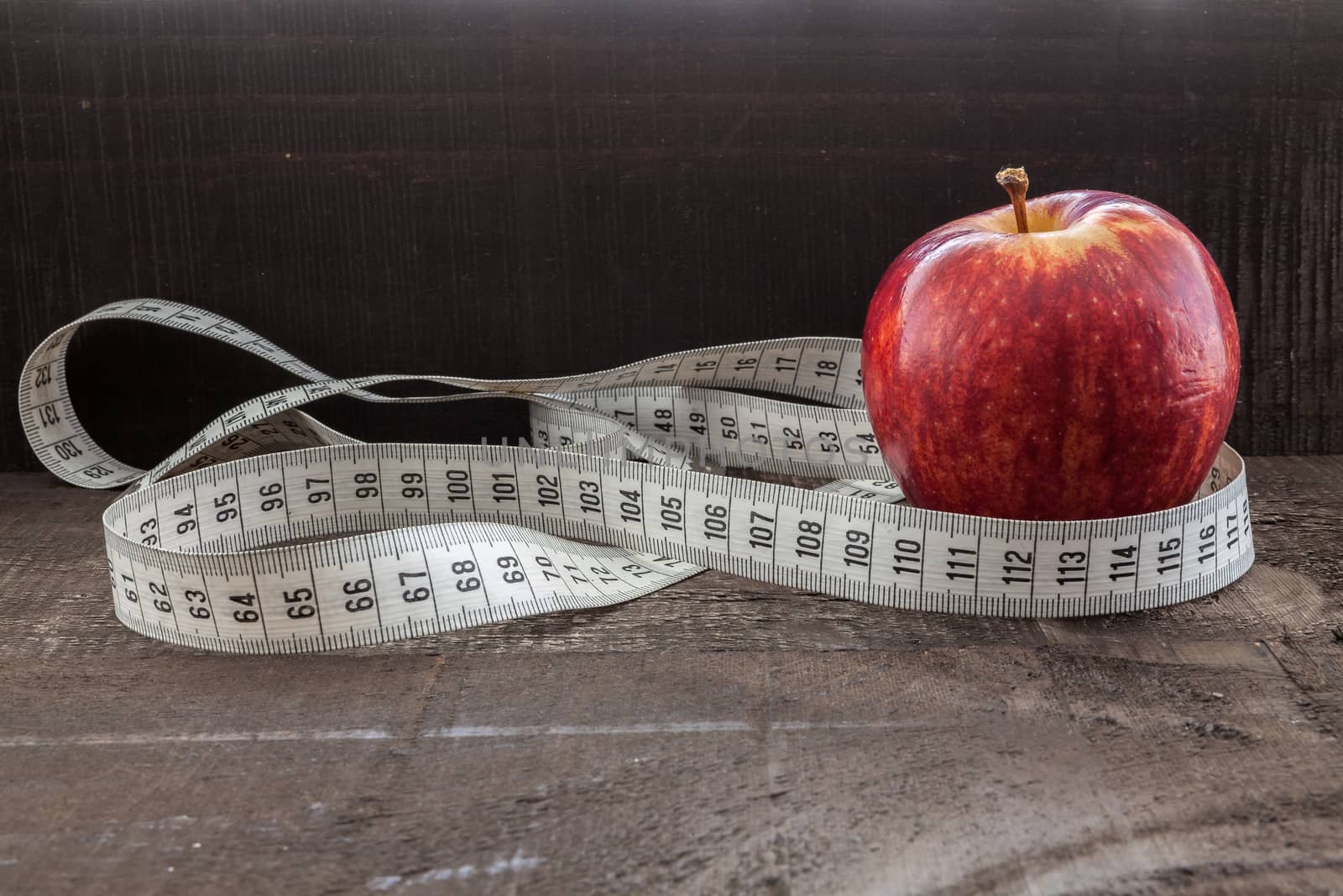 The image shows apple surrounded by a measuring tape referring to diet and health concept on wooden background