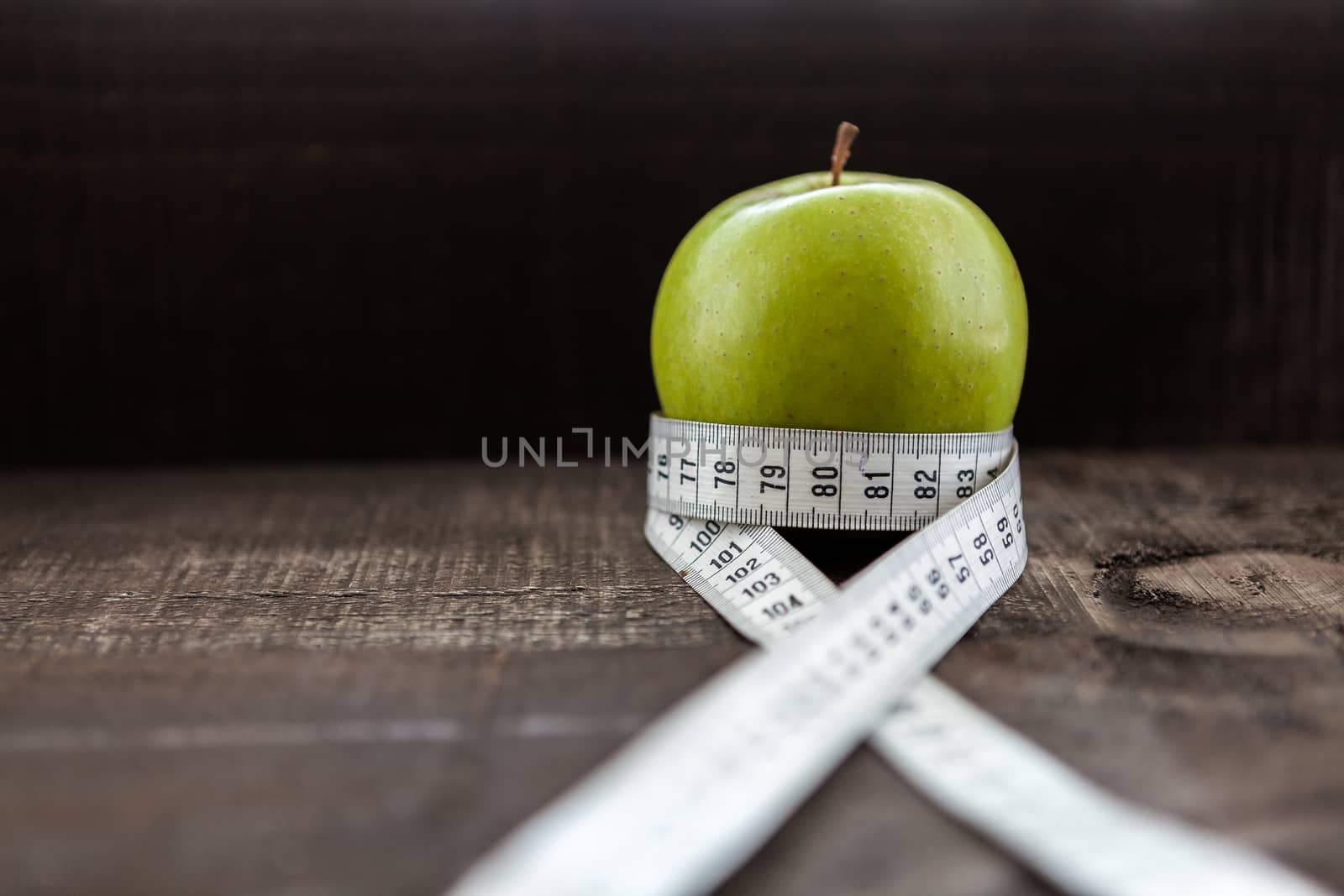 The image shows apple surrounded by a measuring tape referring to diet and health concept on wooden background