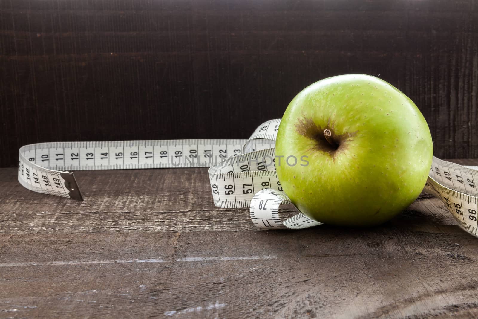 The image shows apple surrounded by a measuring tape referring to diet and health concept on wooden background