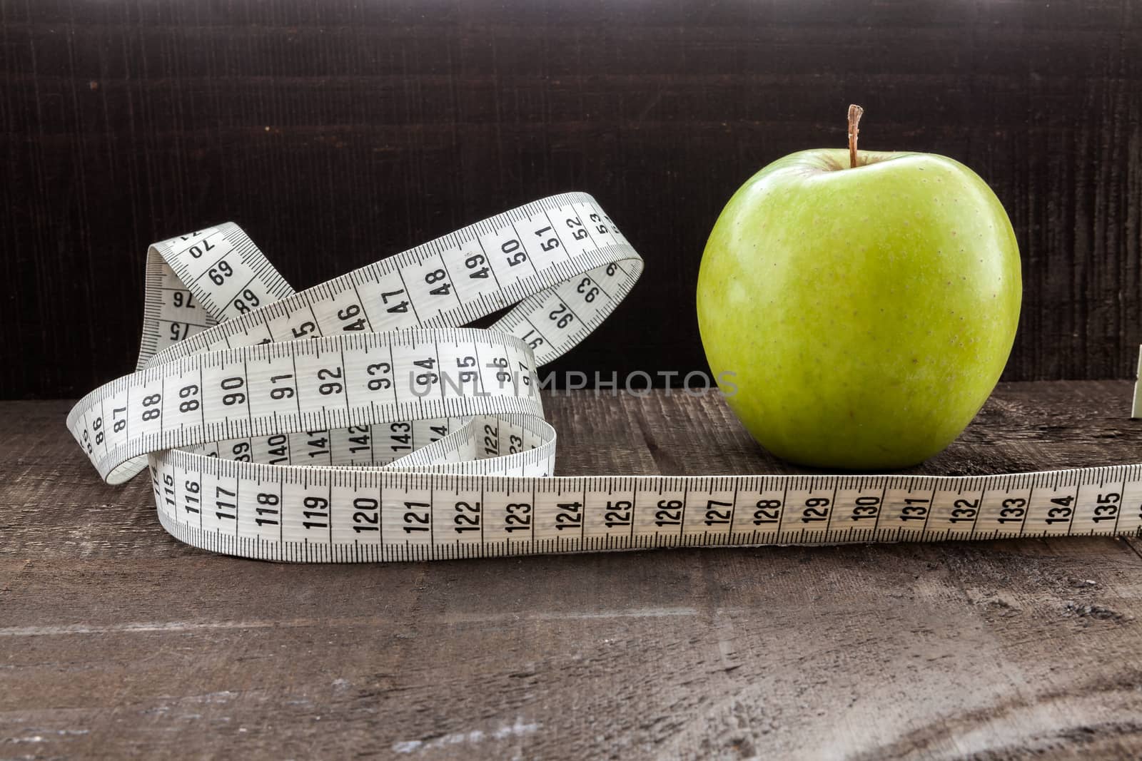 The image shows apple surrounded by a measuring tape referring to diet and health concept on wooden background