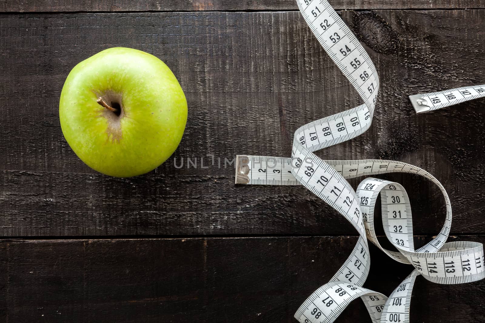 The image shows apple surrounded by a measuring tape referring to diet and health concept on wooden background