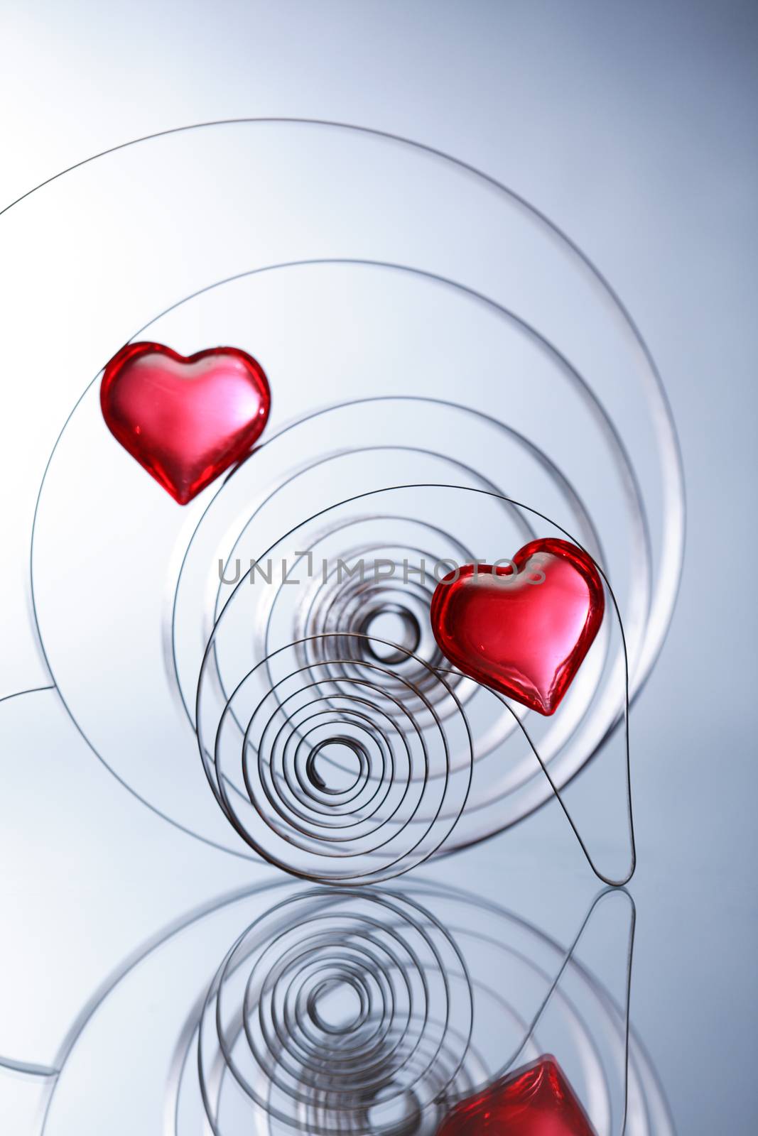 Love concept. Two red glass hearts inside metal springs on nice gray background