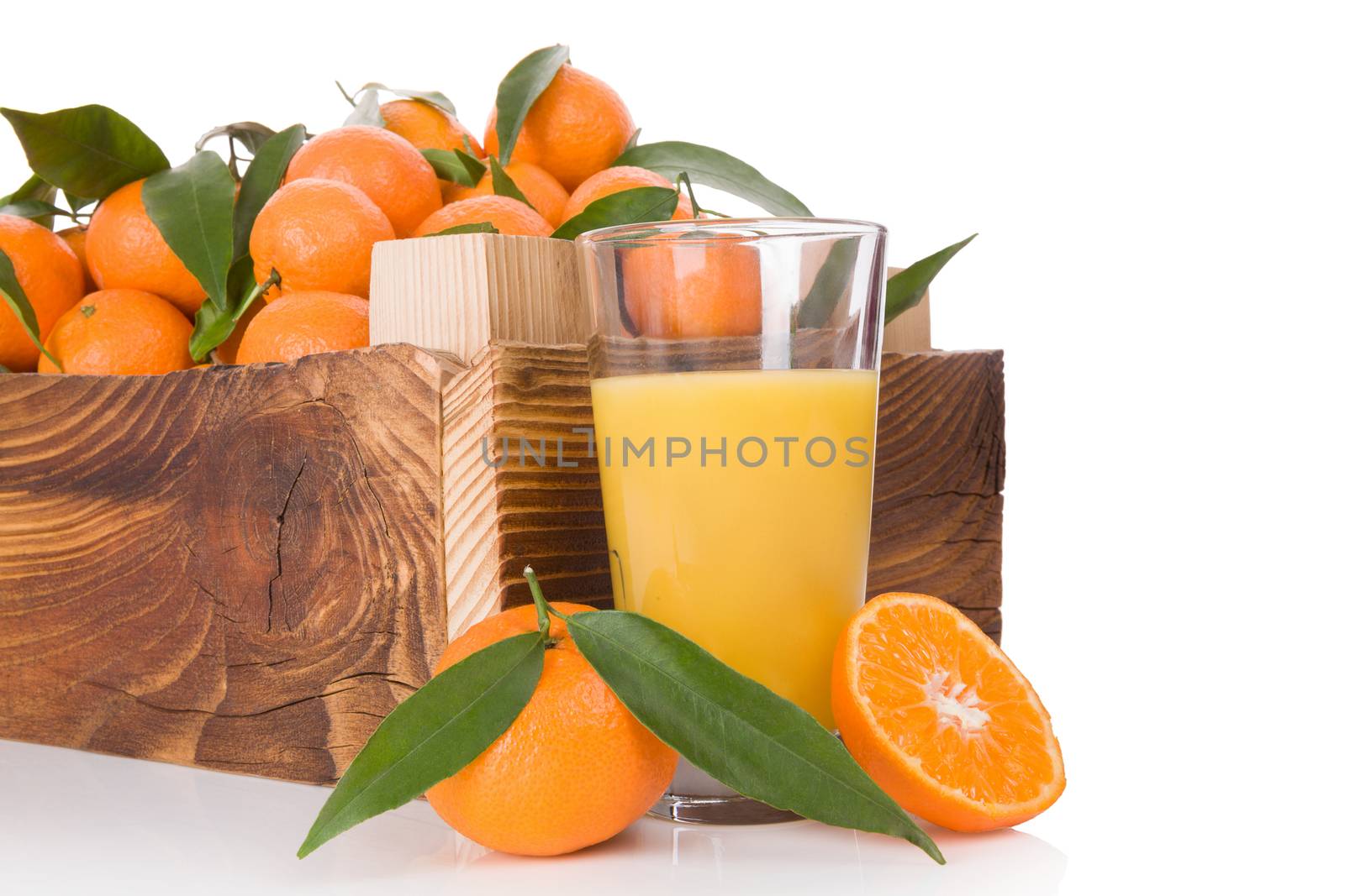 Fresh juice and ripe mandarines with green leaves in wooden crate. Organic fresh mandarines, healthy fruit eating. 
