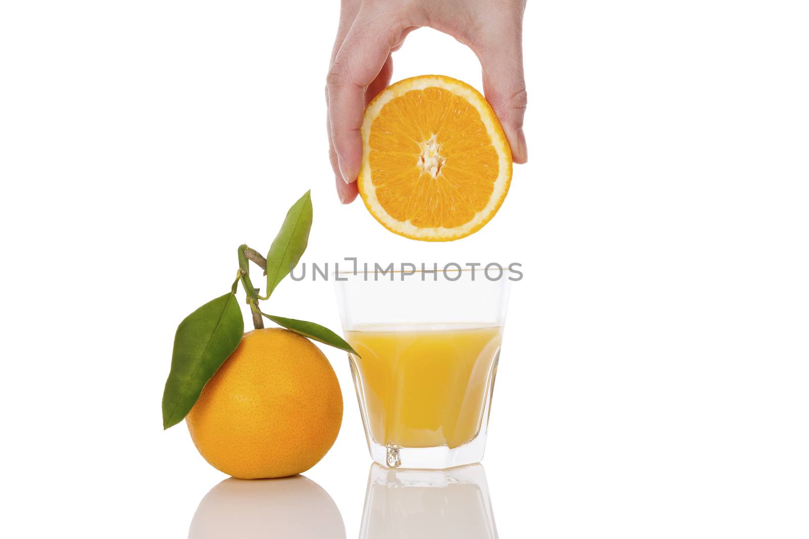 Freshly squeezed orange juice. Female hand squeezing orange into a glass isolated on white background. Healthy juice drink.  