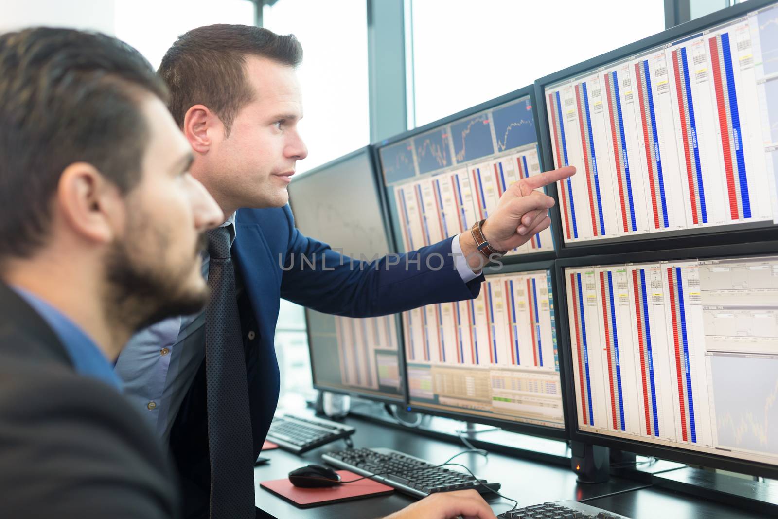 Businessmen trading stocks. Stock traders looking at graphs, indexes and numbers on multiple computer screens. Colleagues in discussion in traders office. Business success concept.