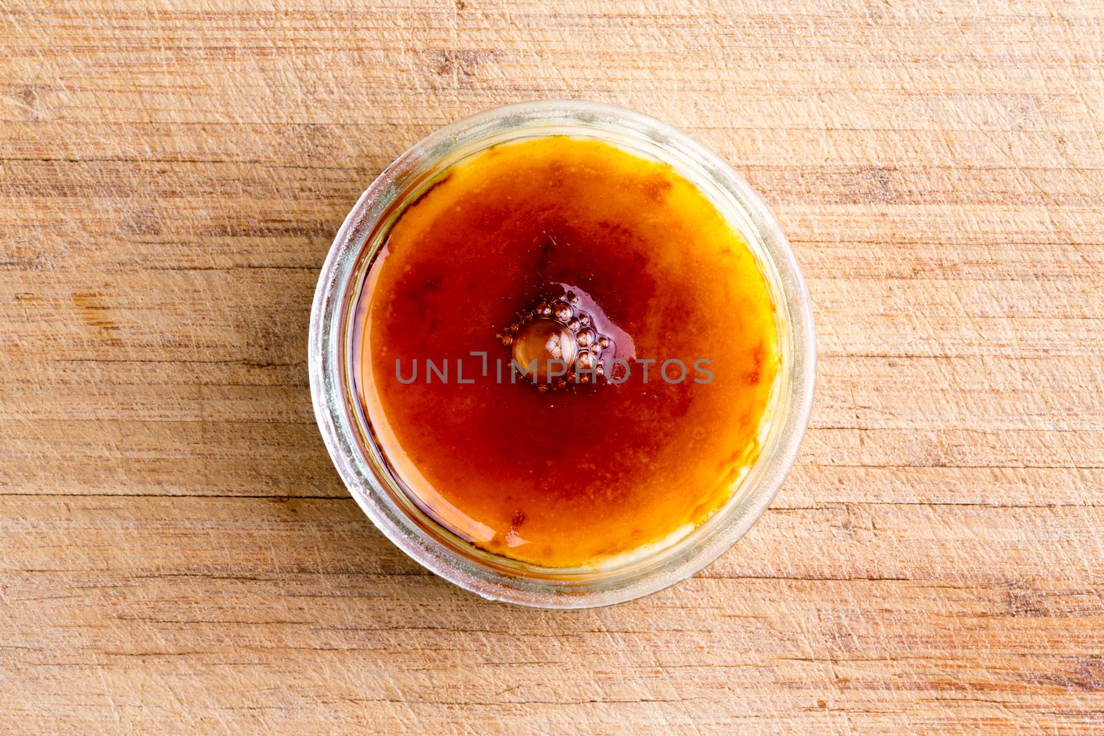 Creme brulee topped with crunchy flamed caramelised sugar served in a glass bowl viewed from overhead on a bamboo board