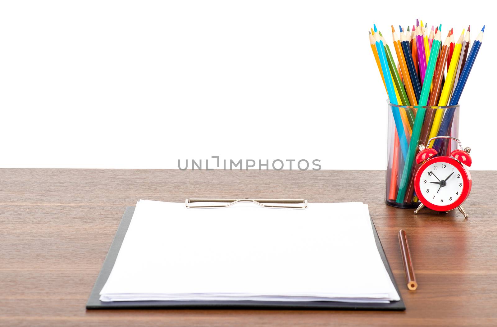 Crayons in pencil cup with folder and alarm clock on table isolated on white background