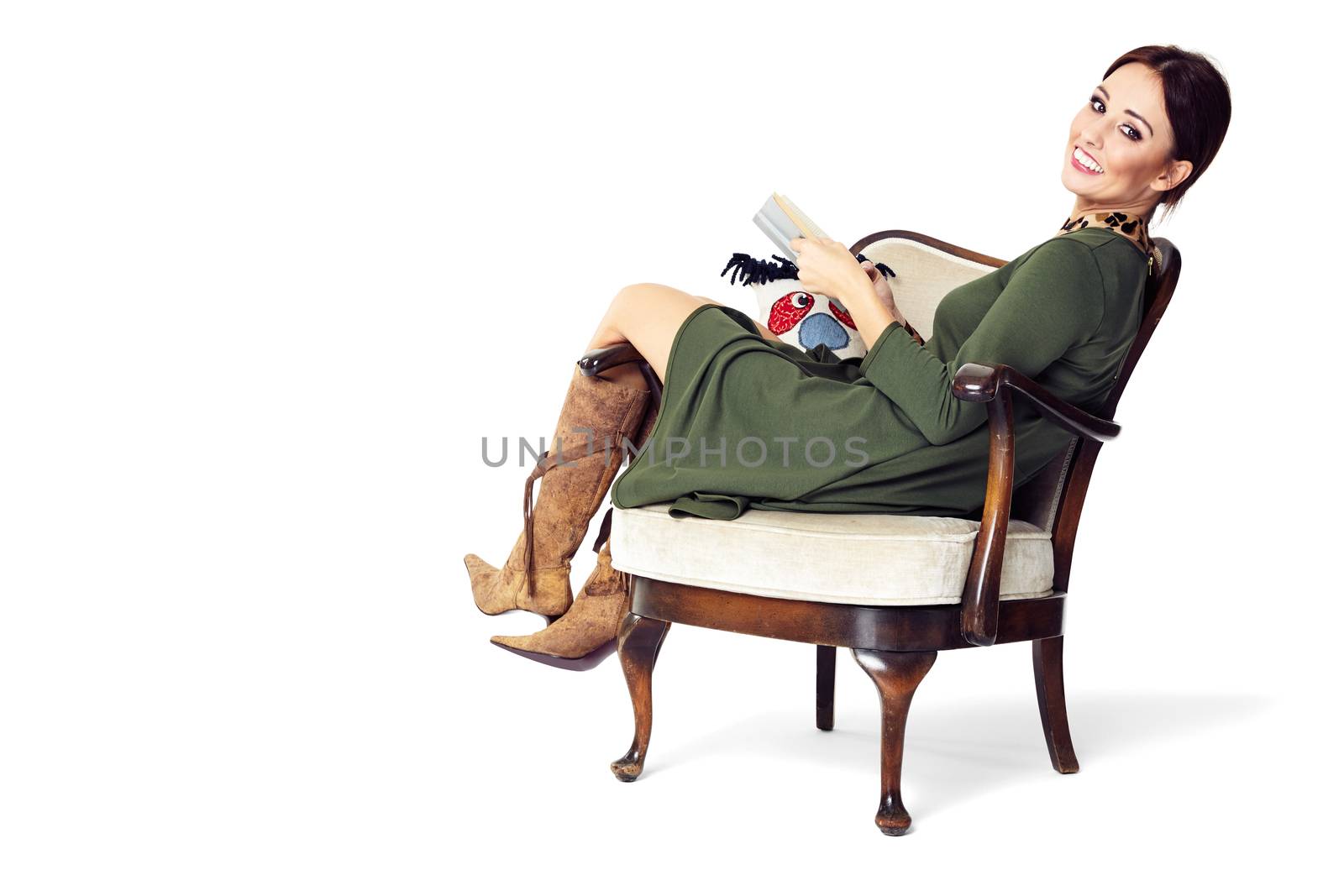 Young woman sitting on chair, holding a book and looking at you.