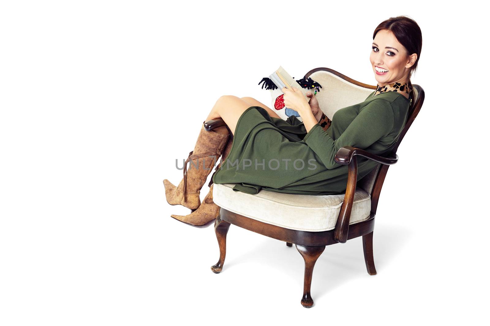 Young woman sitting on chair, holding a book and looking at you.