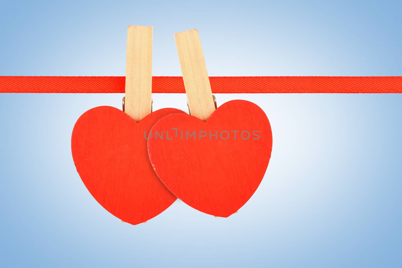 Valentine day template, two red wooden hearts with clothes pins on textile ribbon over sky blue grain noise gradient
