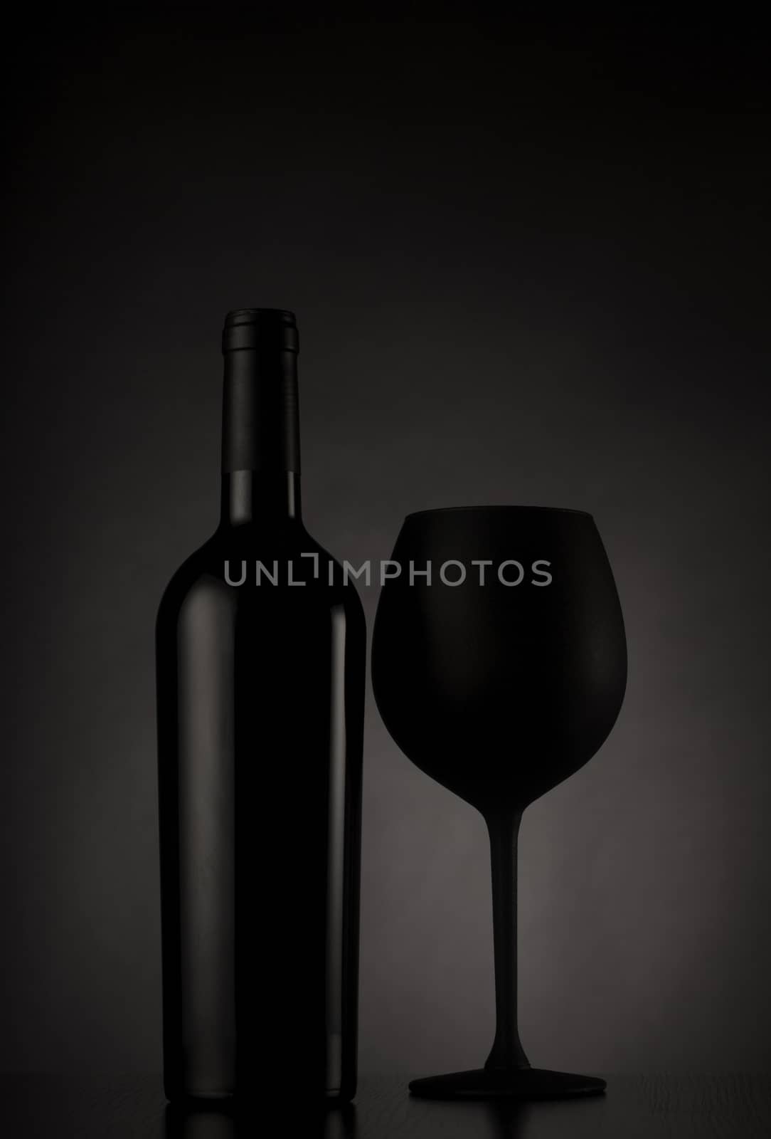 Black wine bottle and black glass of wine on black background