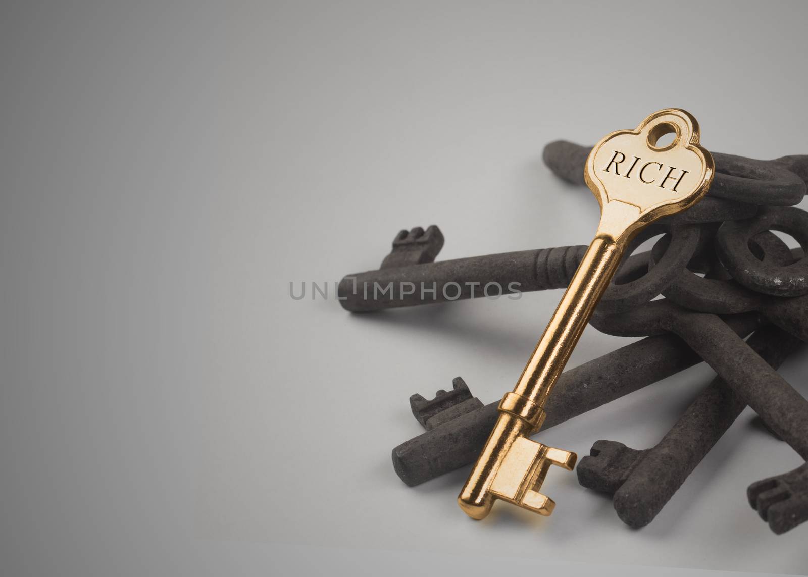 A golden key sitting on top of some rusted ones with the word rich engraved on it