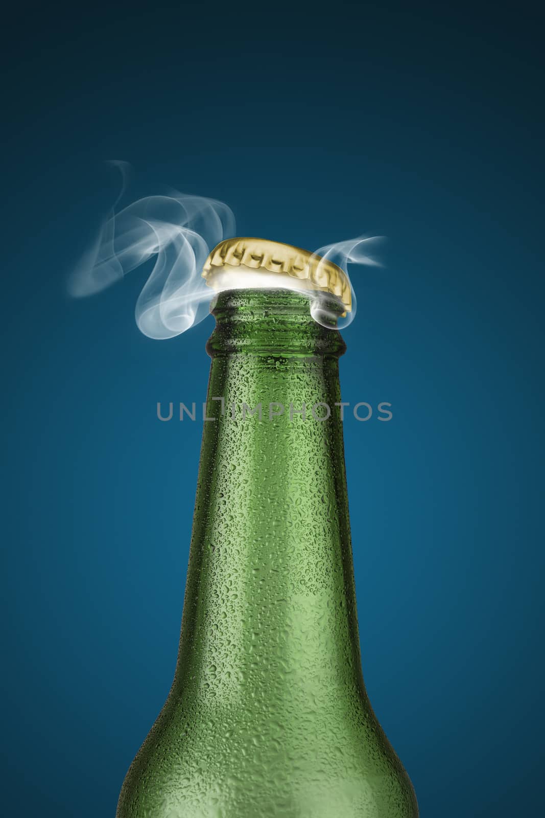 Green cold beer bottle with water drops and golden cap open on blue background