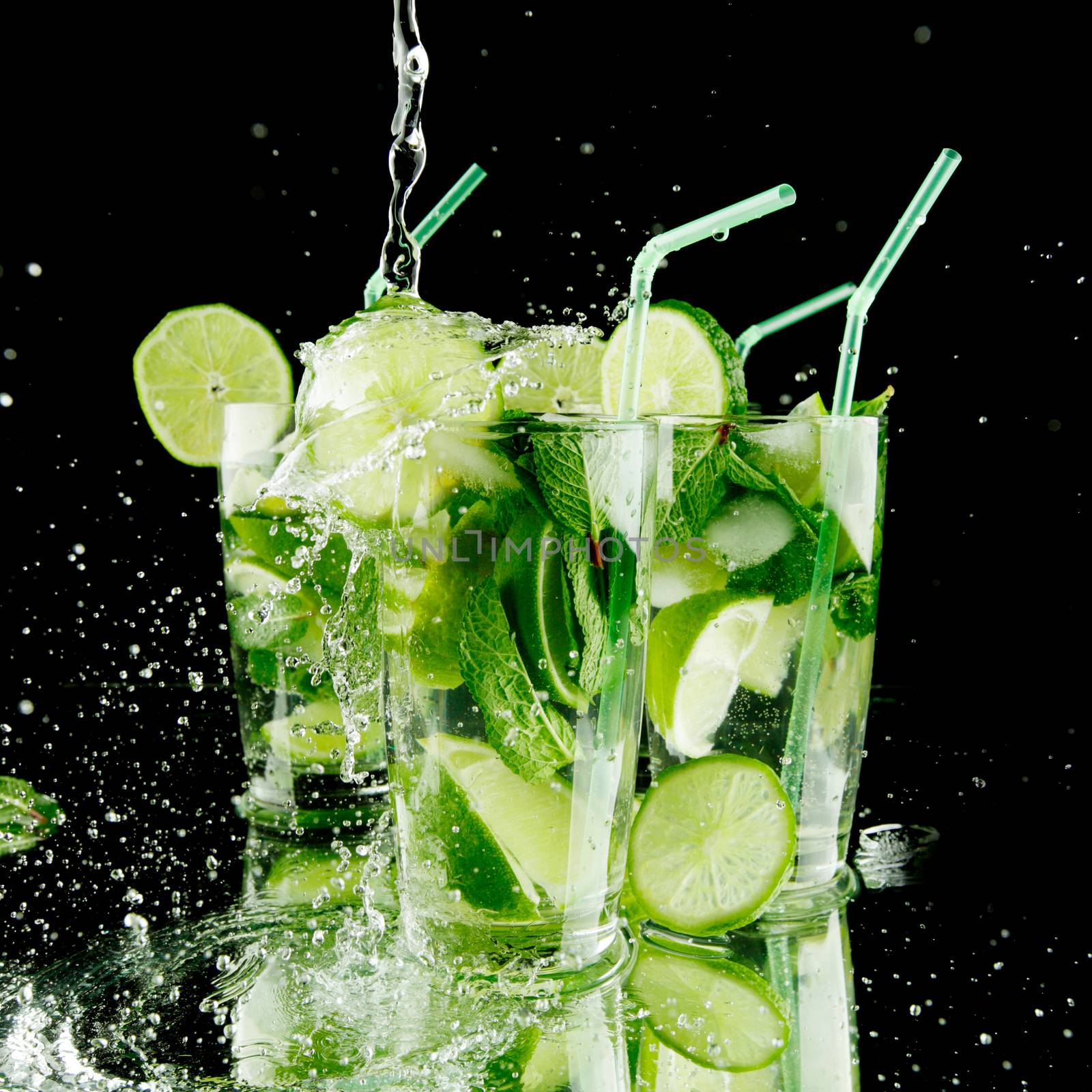 Pouring fresh mojito cocktail in glasses isolated on black background