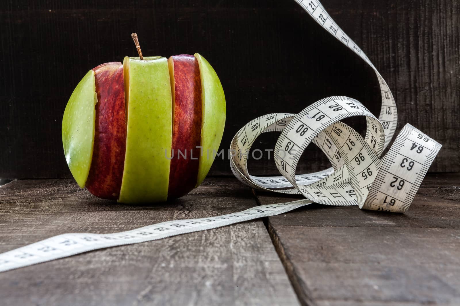 The image shows apple surrounded by a measuring tape referring to diet and health concept on wooden background