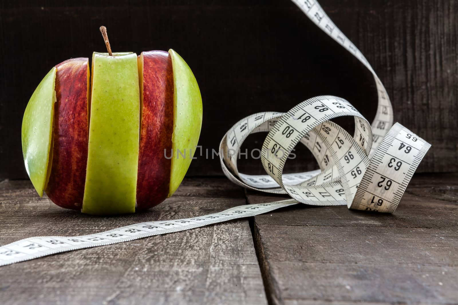 The image shows apple surrounded by a measuring tape referring to diet and health concept on wooden background