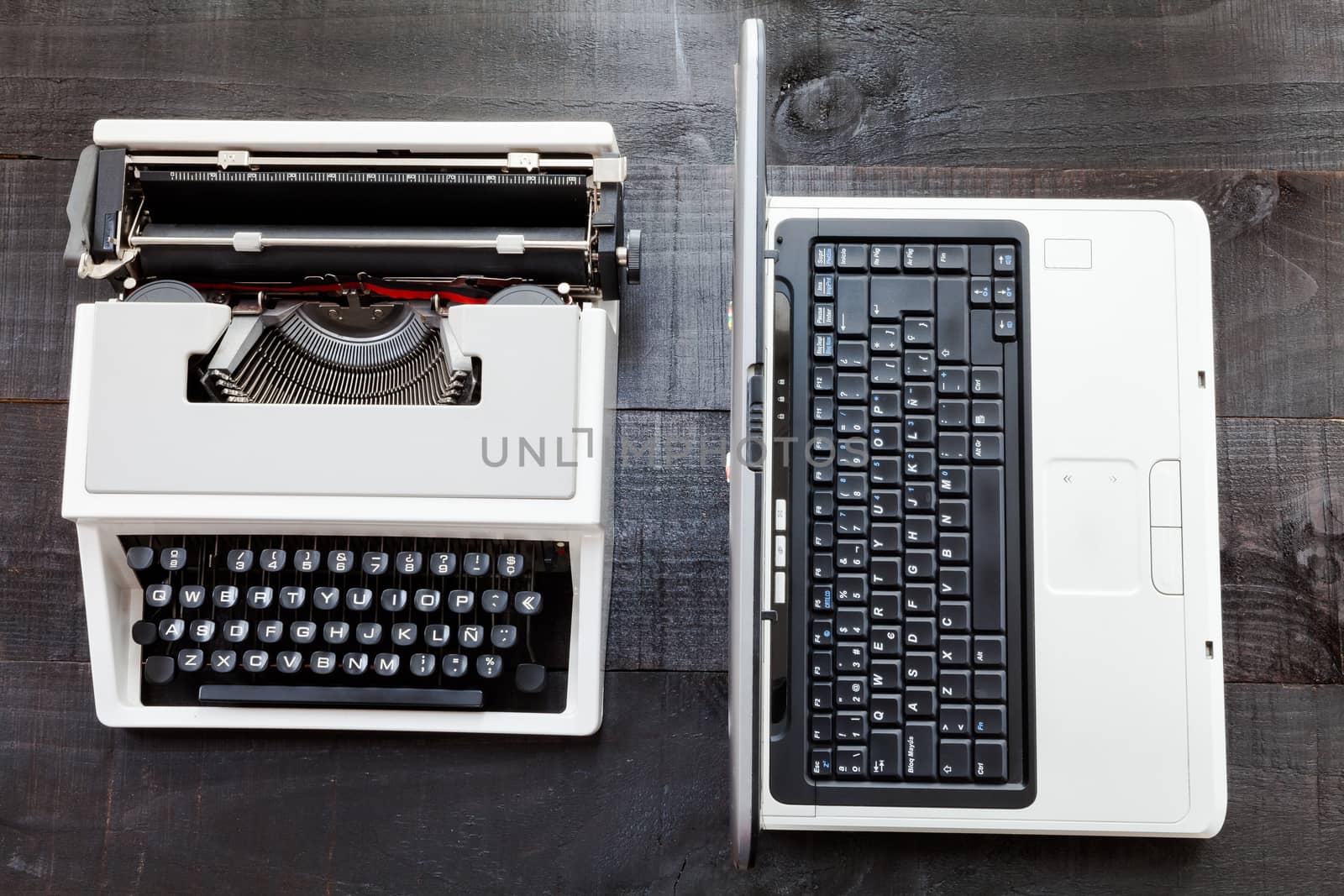 The image represents a retro typewriter and a laptop on a dark wood background conceptualizing that the time of technology is getting older the picture is taken from a top view